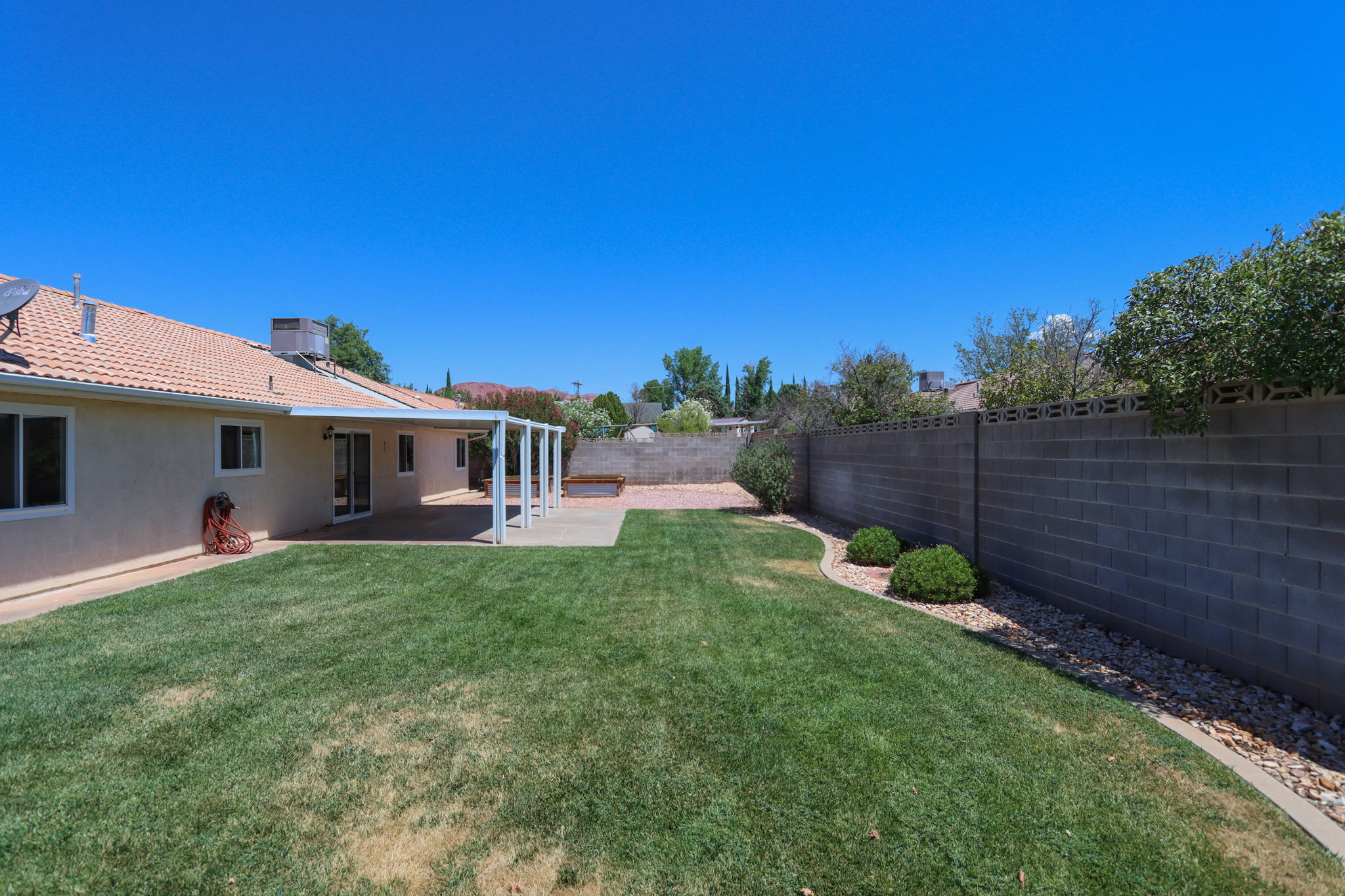 Expansive backyard featuring a large green lawn, concrete patio with pergola, block wall perimeter, and rock landscaping