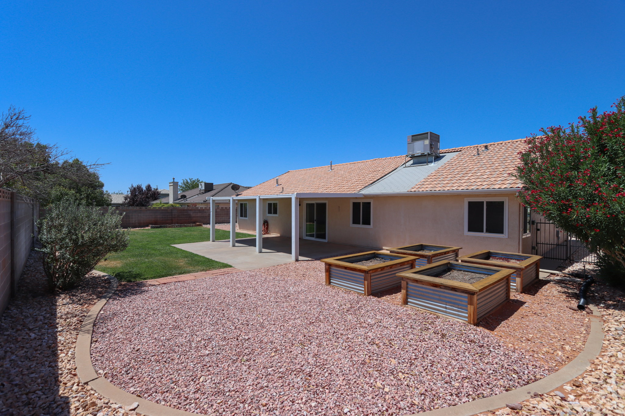 Spacious backyard featuring a covered patio, xeriscaping with decorative rock, a dedicated grassy area, and four raised garden beds