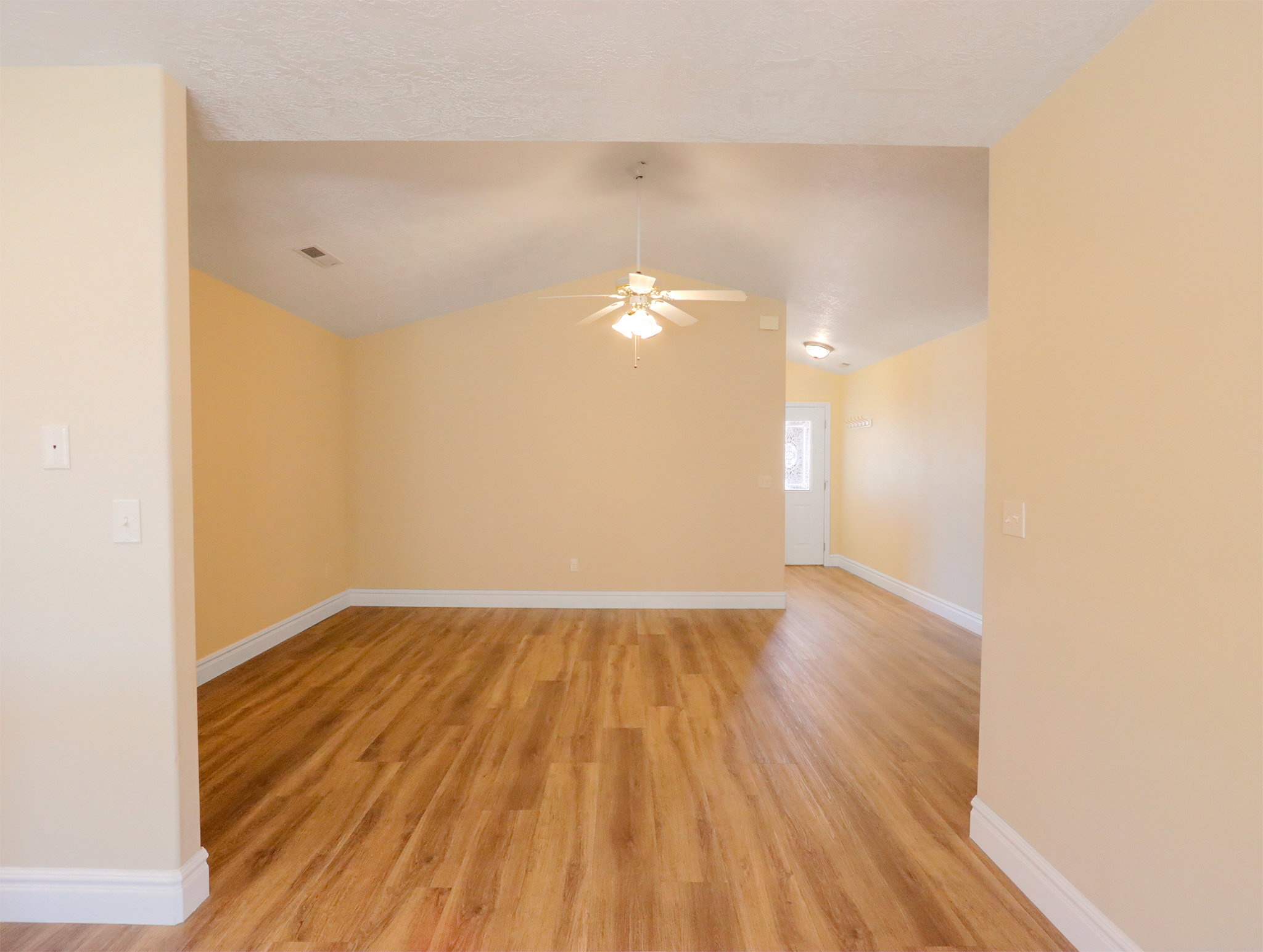 Spacious room featuring vaulted ceilings, wood-finish flooring, and a ceiling fan with integrated lighting