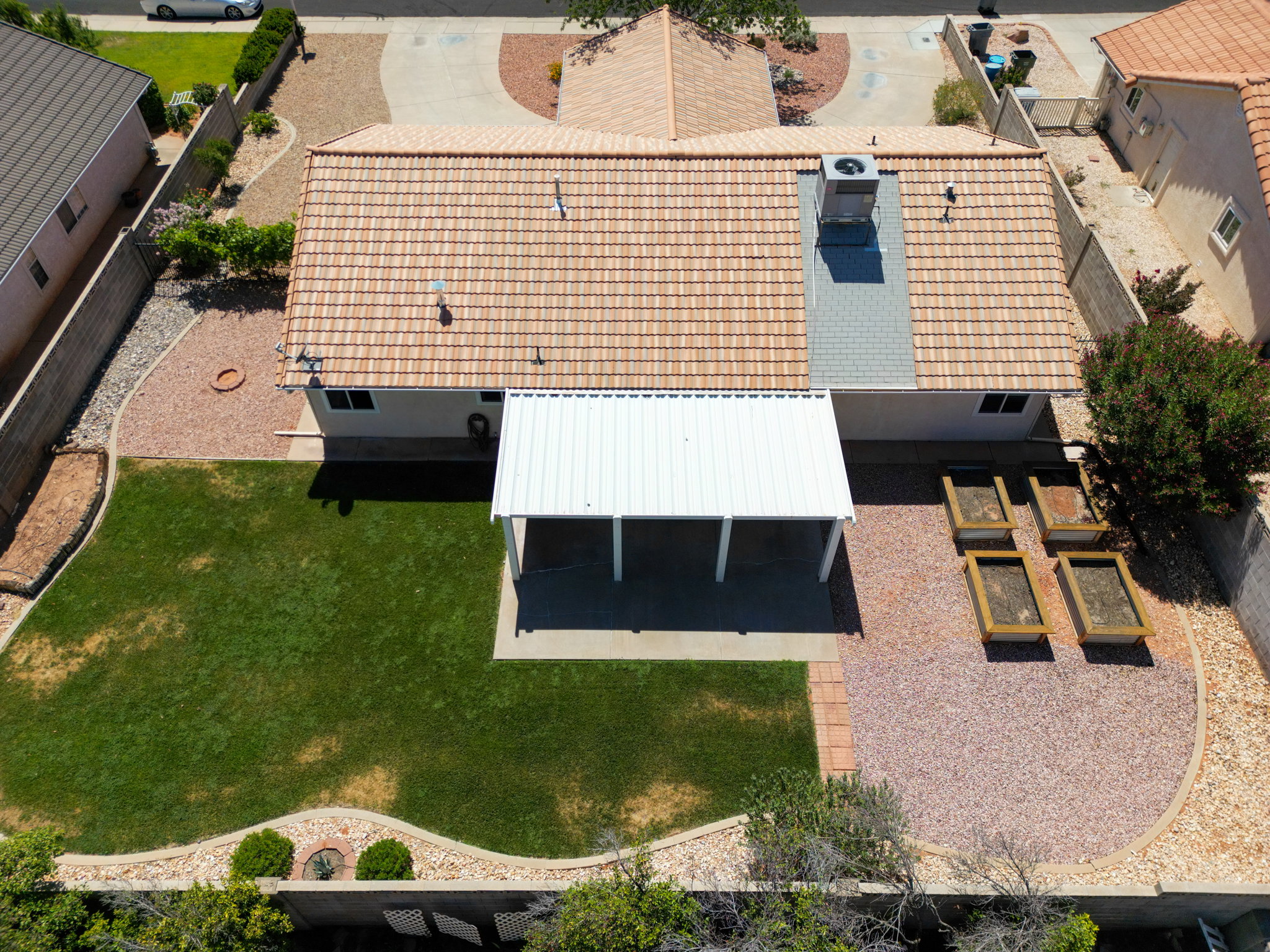 Backyard featuring a covered patio, a manicured lawn, gravel landscaping, and raised garden beds