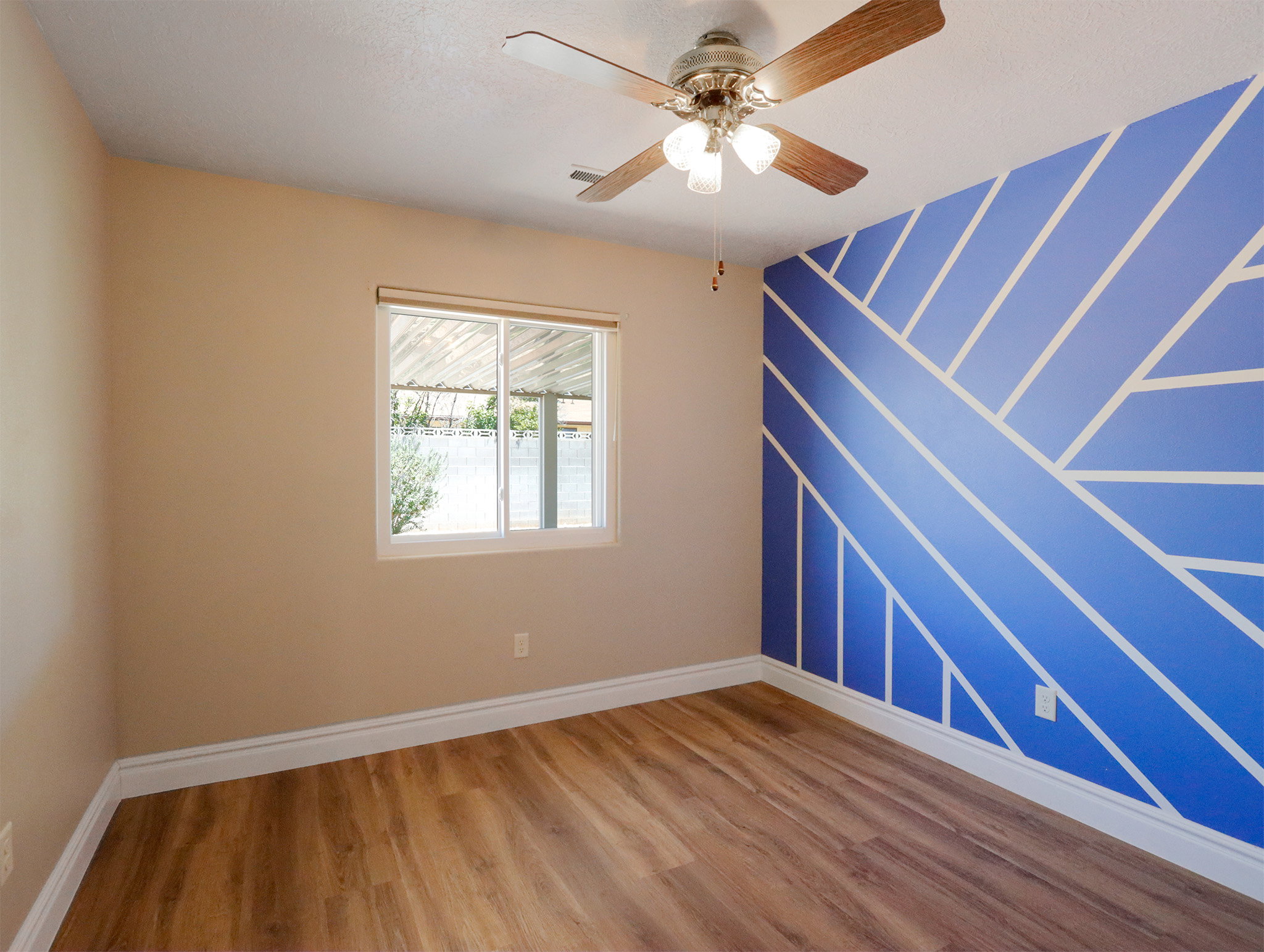 Interior room featuring a blue accent wall with a geometric pattern, wood-finish flooring, and a ceiling fan with integrated lighting