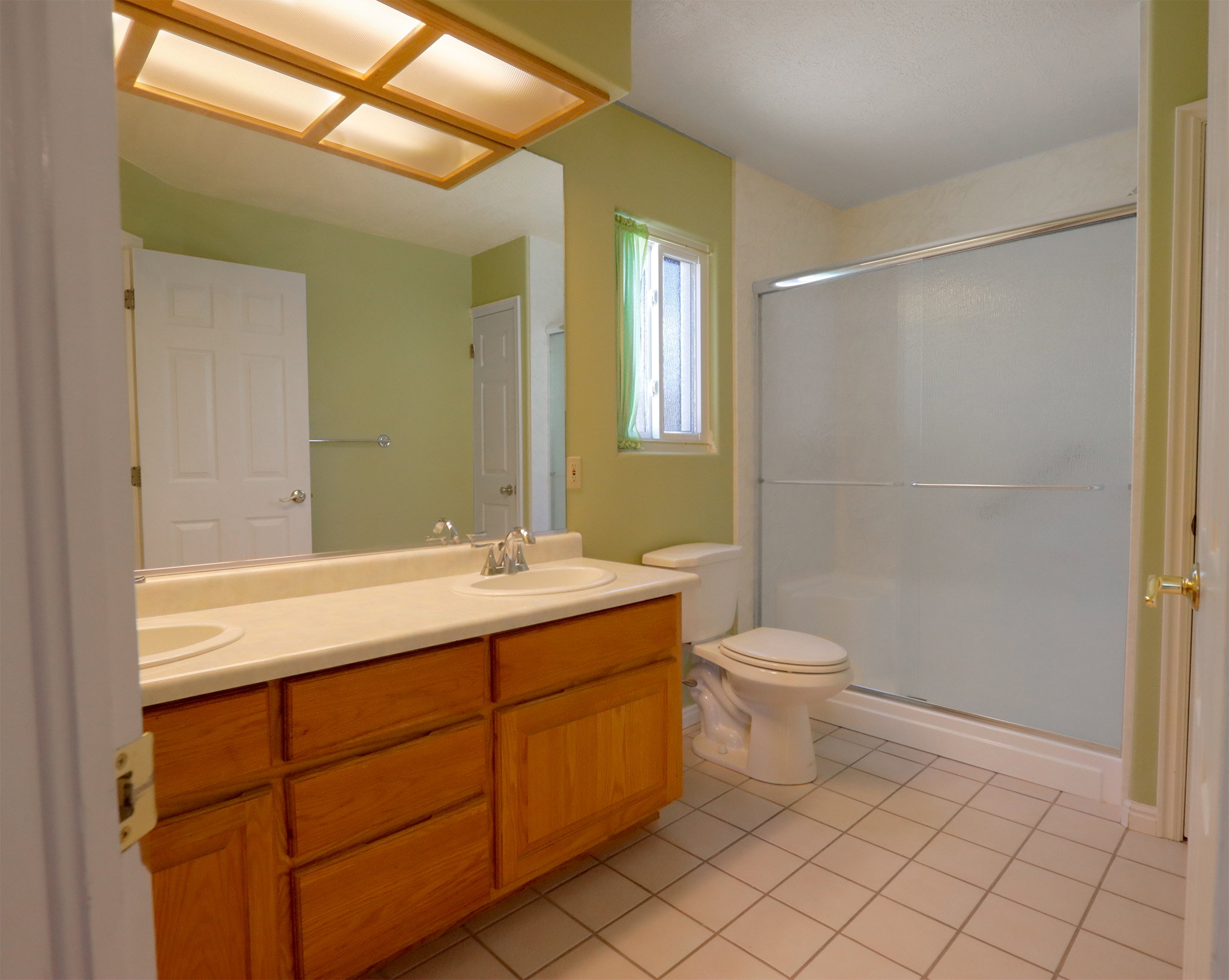 Bathroom featuring a double vanity with light wood cabinetry, a light-colored countertop, and two integrated sinks