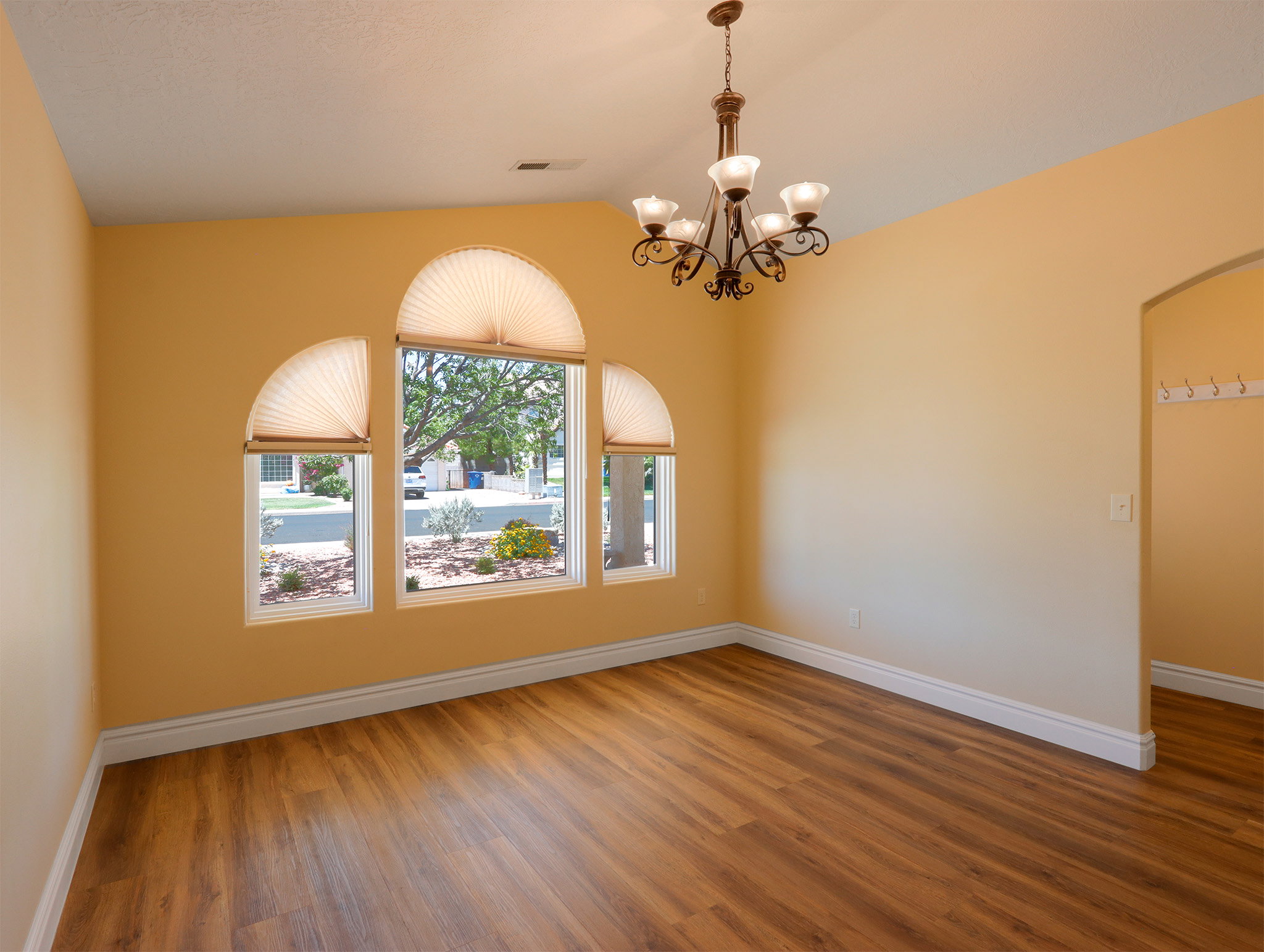 Spacious room featuring wood-finish flooring, a decorative chandelier, and arched windows with pleated shades