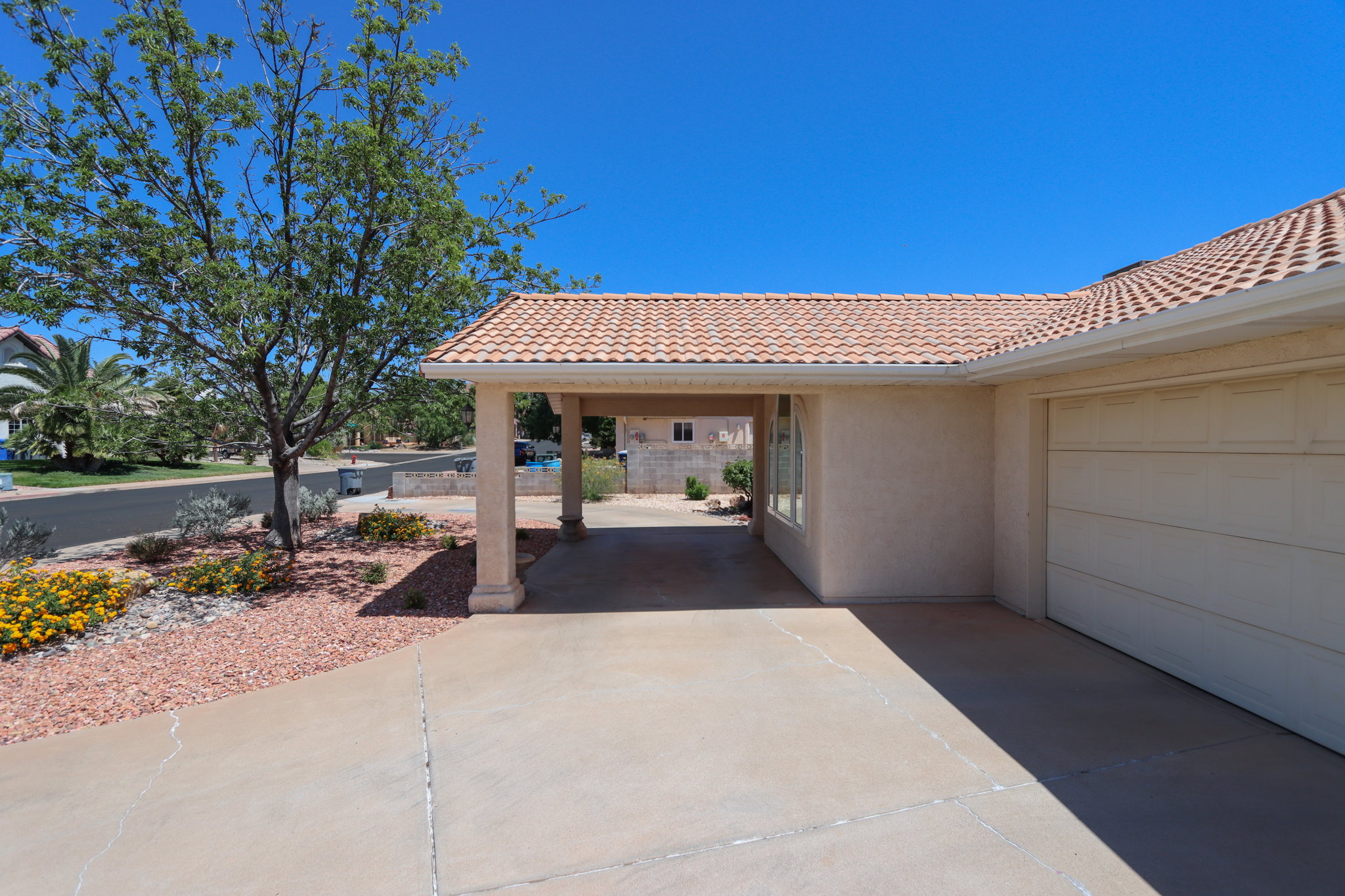 Exterior featuring a tile roof, an attached garage, a covered carport, stucco siding, and a landscaped front yard with decorative rock and plantings
