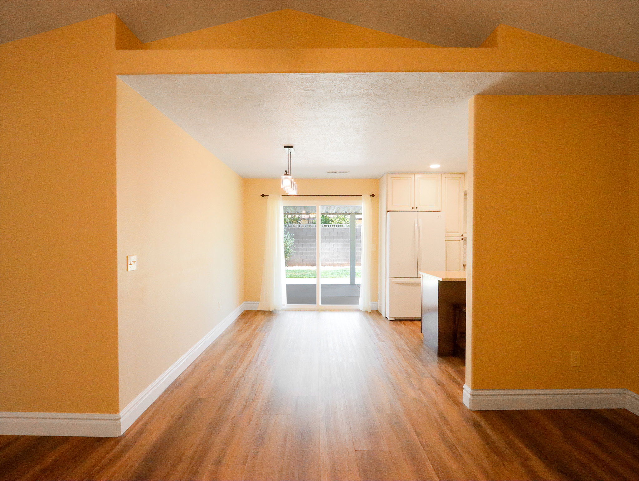 Open-concept living area featuring wood-finish flooring, white baseboards, and a vaulted ceiling detail