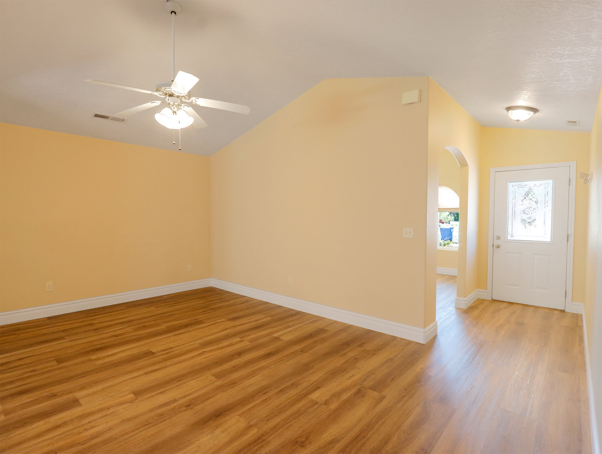 Spacious living area featuring wood-finish flooring, vaulted ceilings, and a ceiling fan with integrated lighting