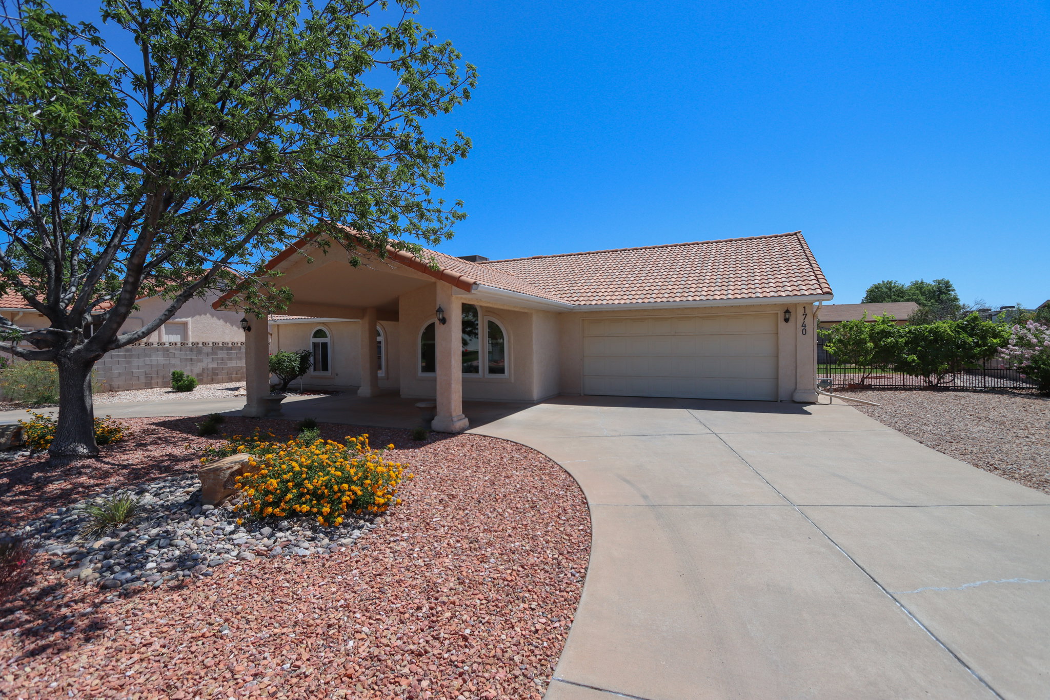 Southwestern-style residence featuring a prominent covered entryway with columns, a tiled roof, and a two-car garage