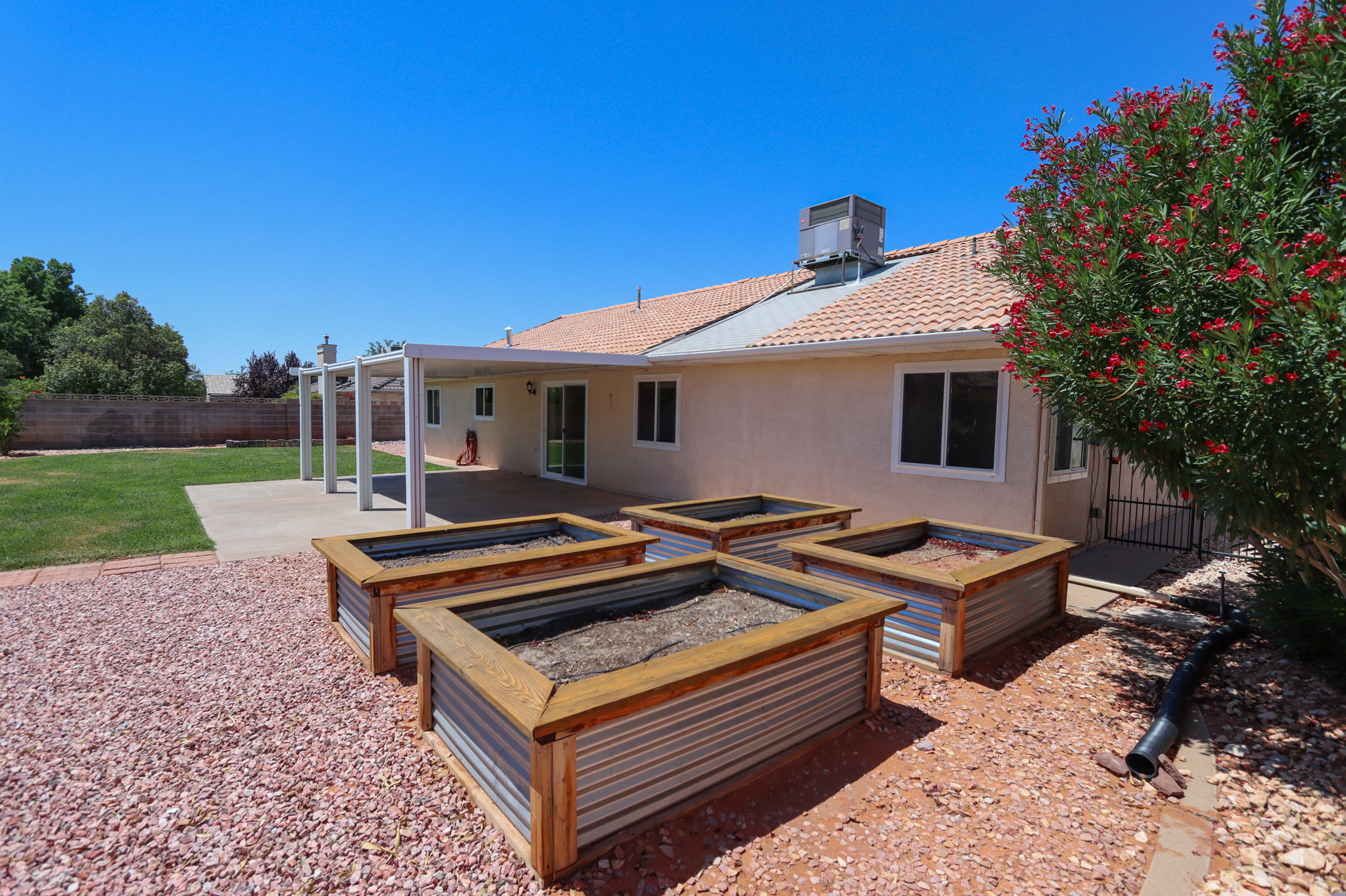 Backyard featuring a covered patio, multiple raised garden beds with corrugated metal and wood-finish construction, and a manicured lawn area