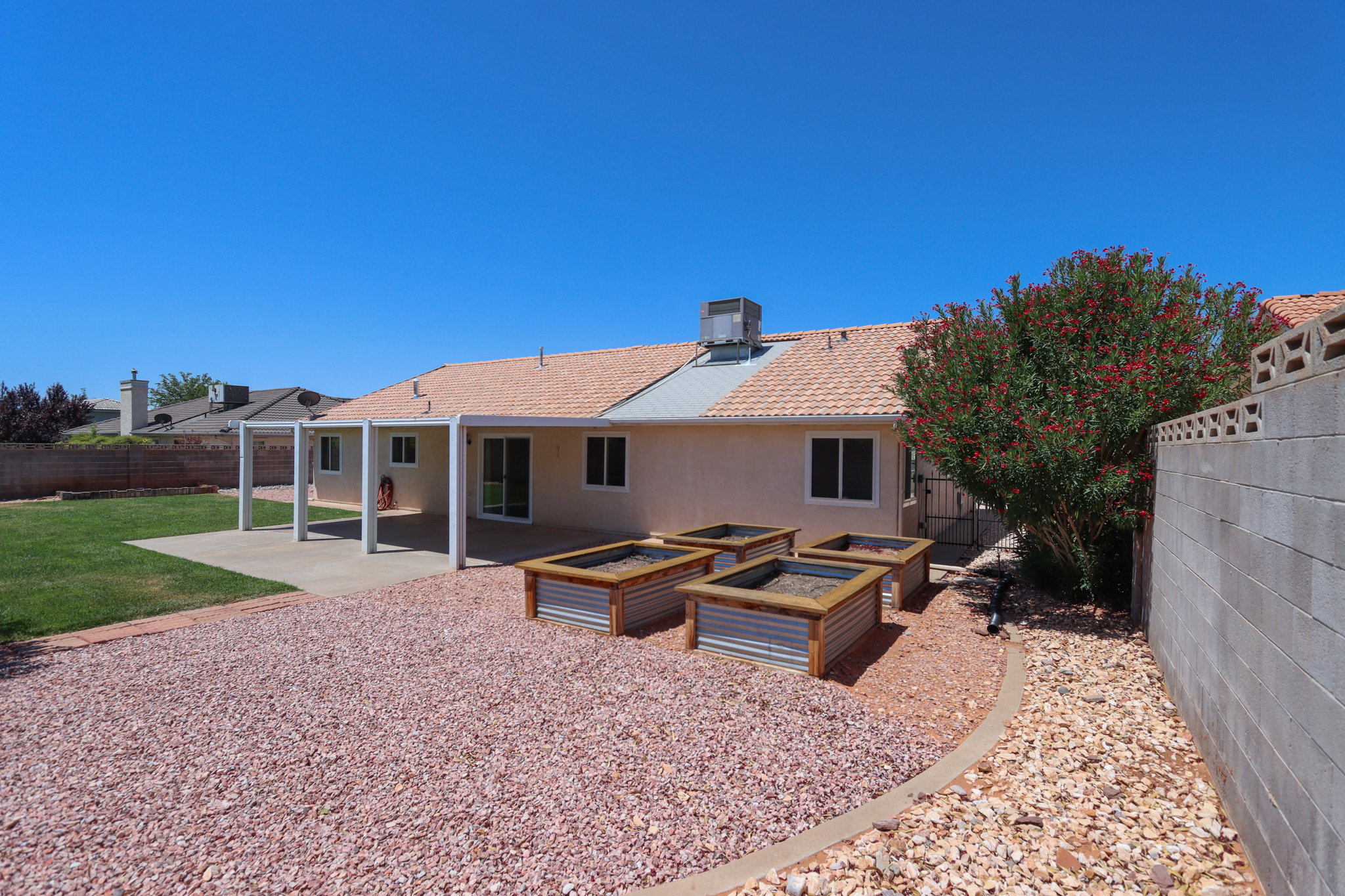 Expansive backyard featuring a covered patio, multiple raised garden beds, a large grassy area, and a mature flowering shrub