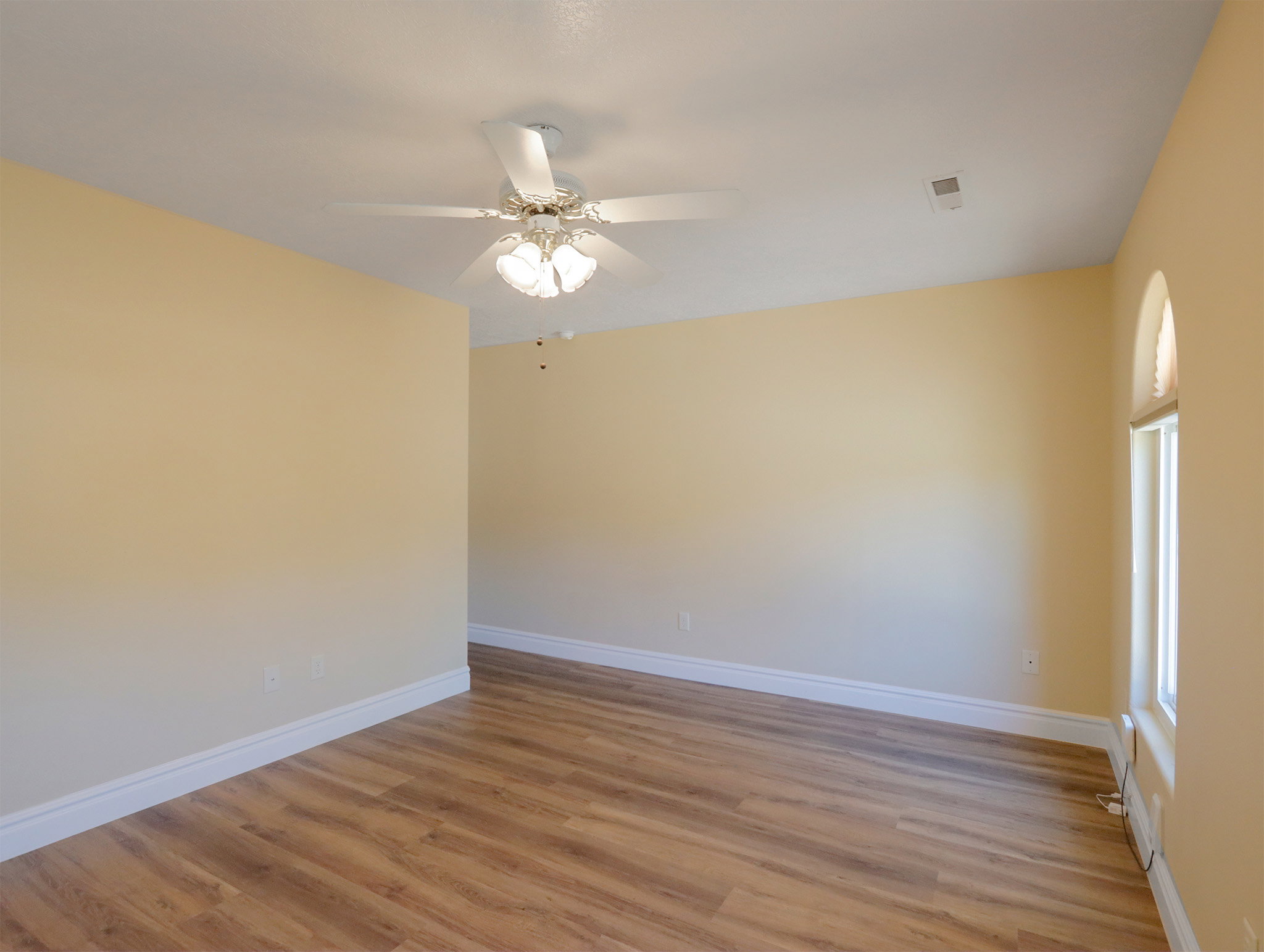 Spacious room featuring wood-finish flooring, vaulted ceiling, and a ceiling fan with integrated lighting