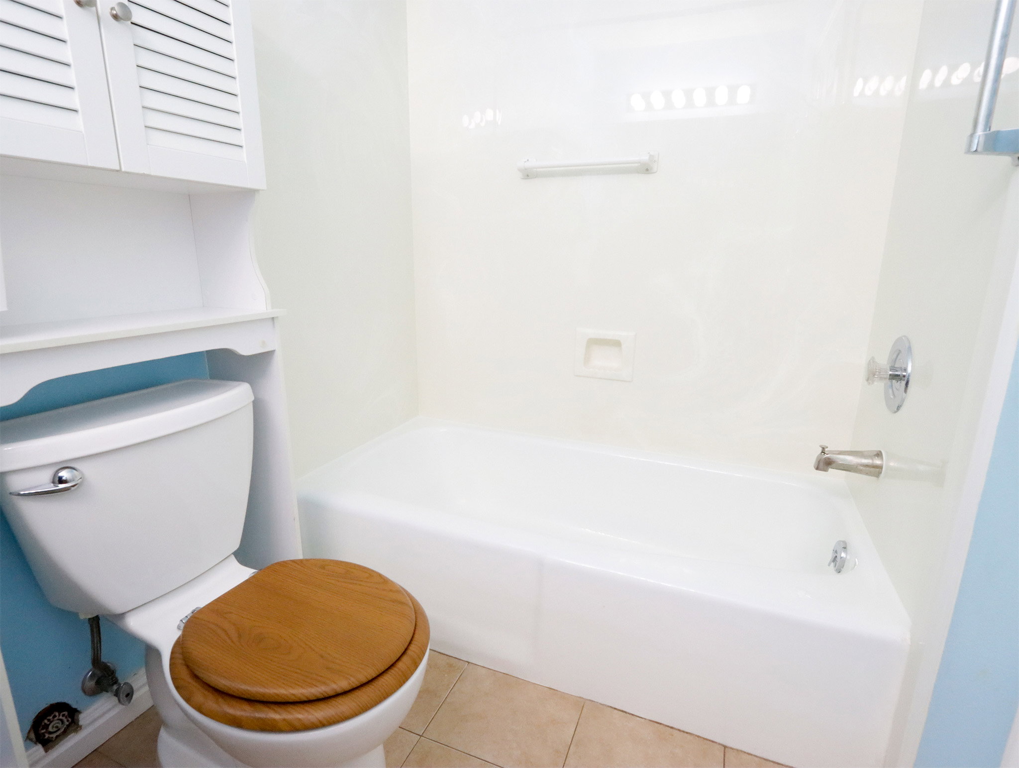 Bathroom featuring a white bathtub, ceramic tile flooring, and a white toilet with a wood-finish seat