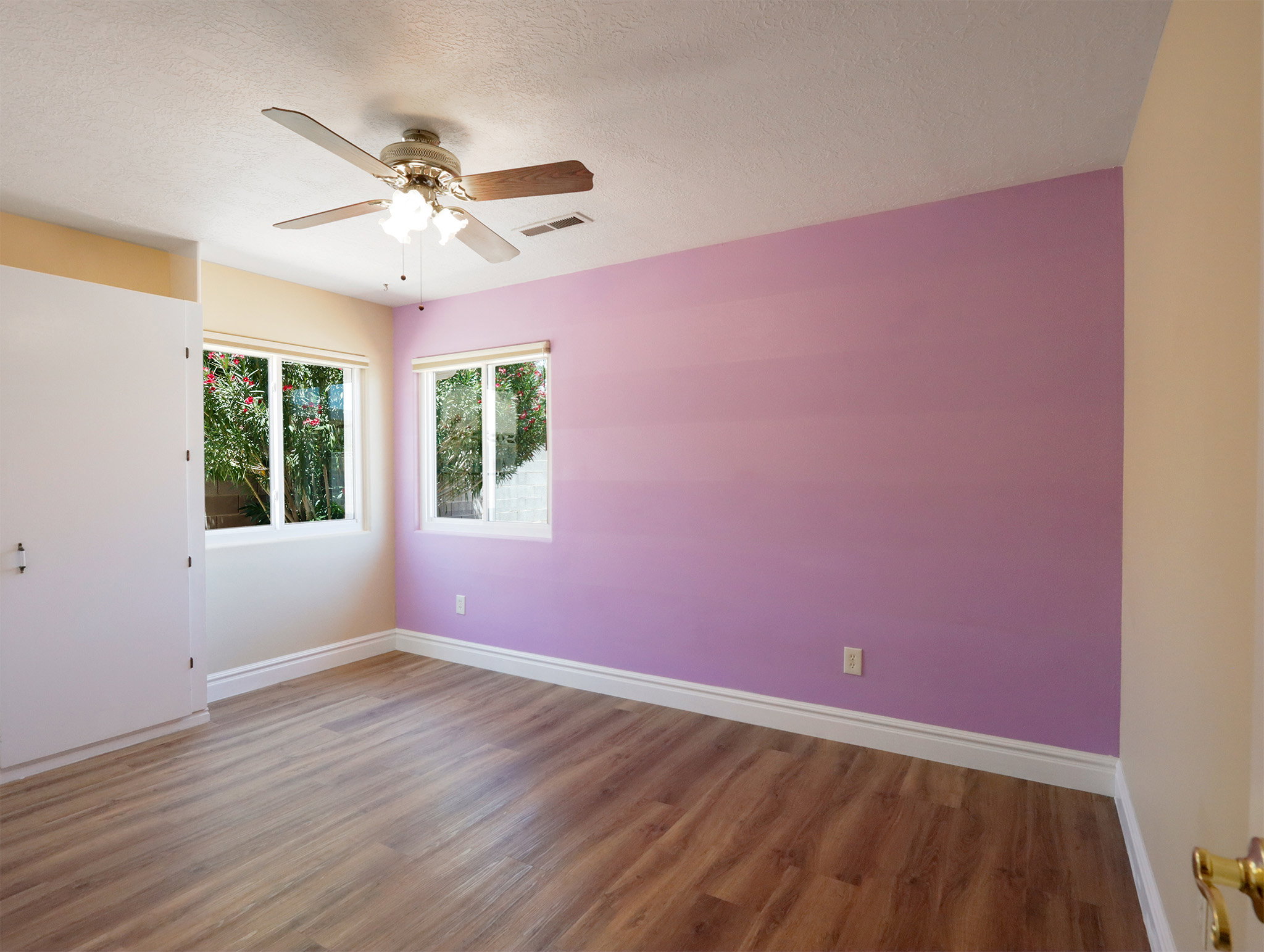 Room featuring wood-finish flooring, two window openings, and a ceiling fan with light fixture