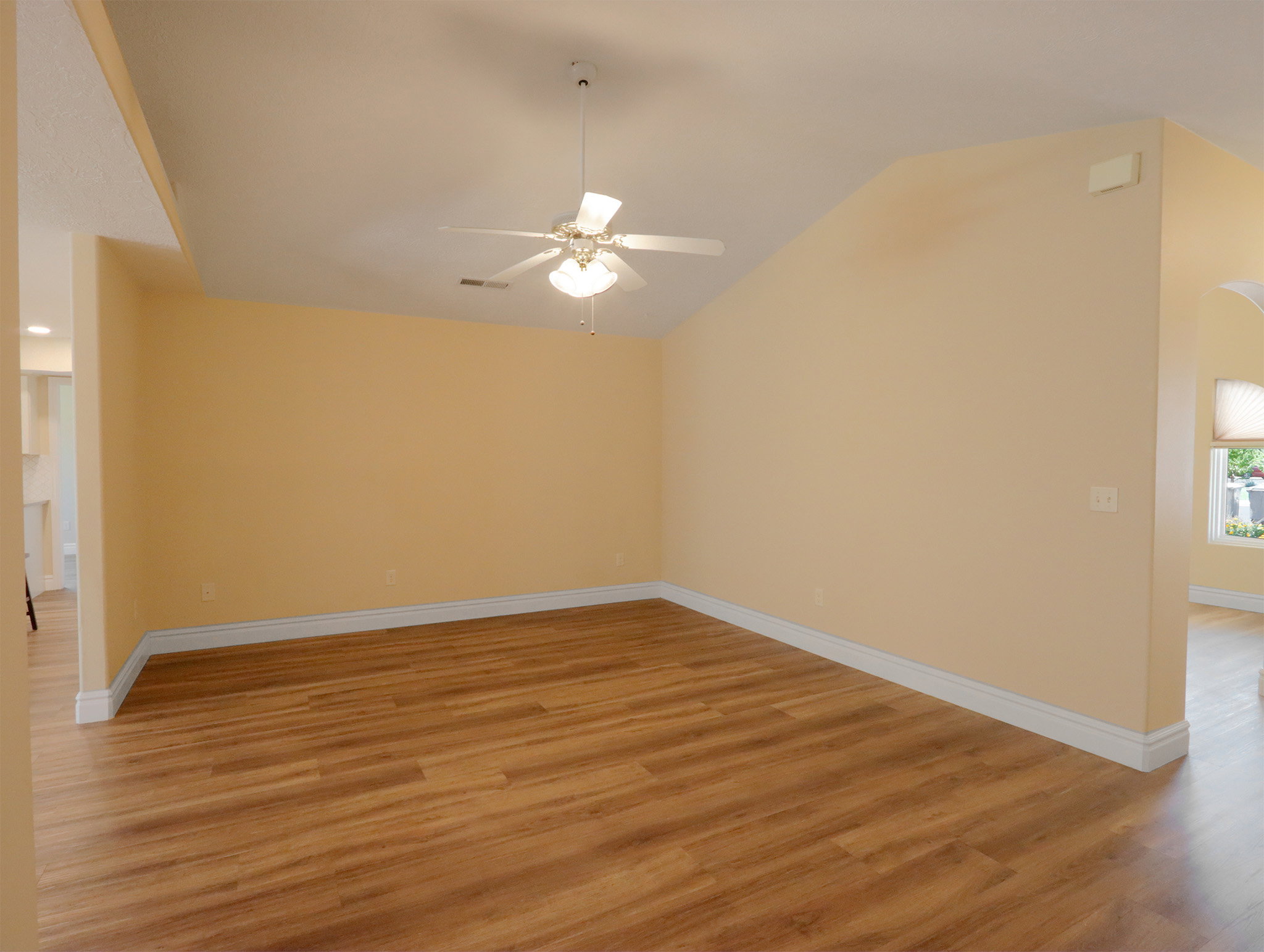 Spacious interior featuring wood-finish flooring, vaulted ceiling, a ceiling fan with integrated lighting, and white baseboards