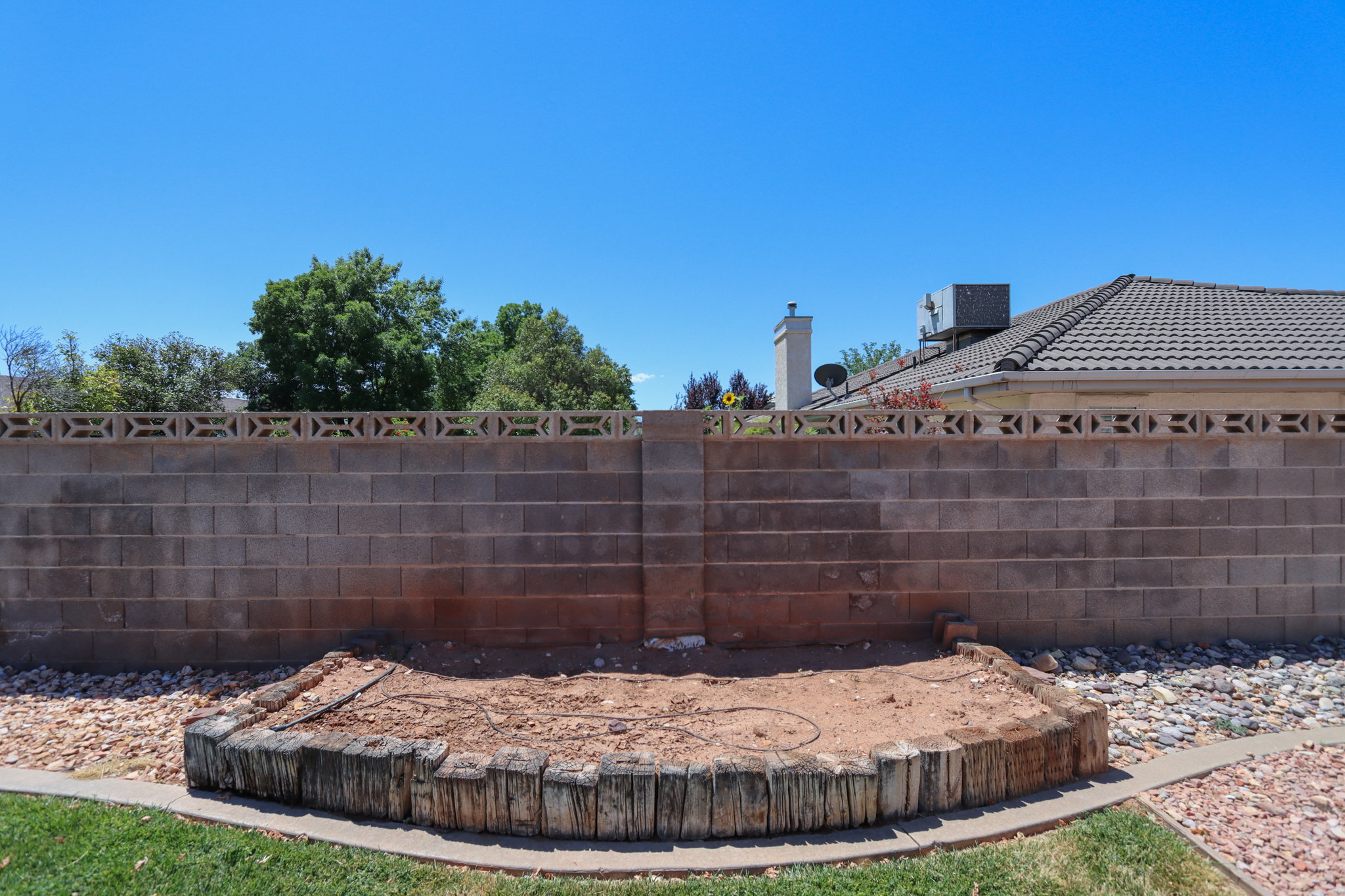 Outdoor space featuring a concrete block privacy wall with decorative top blocks, a semicircular planter with wood log edging, and a rock-covered area
