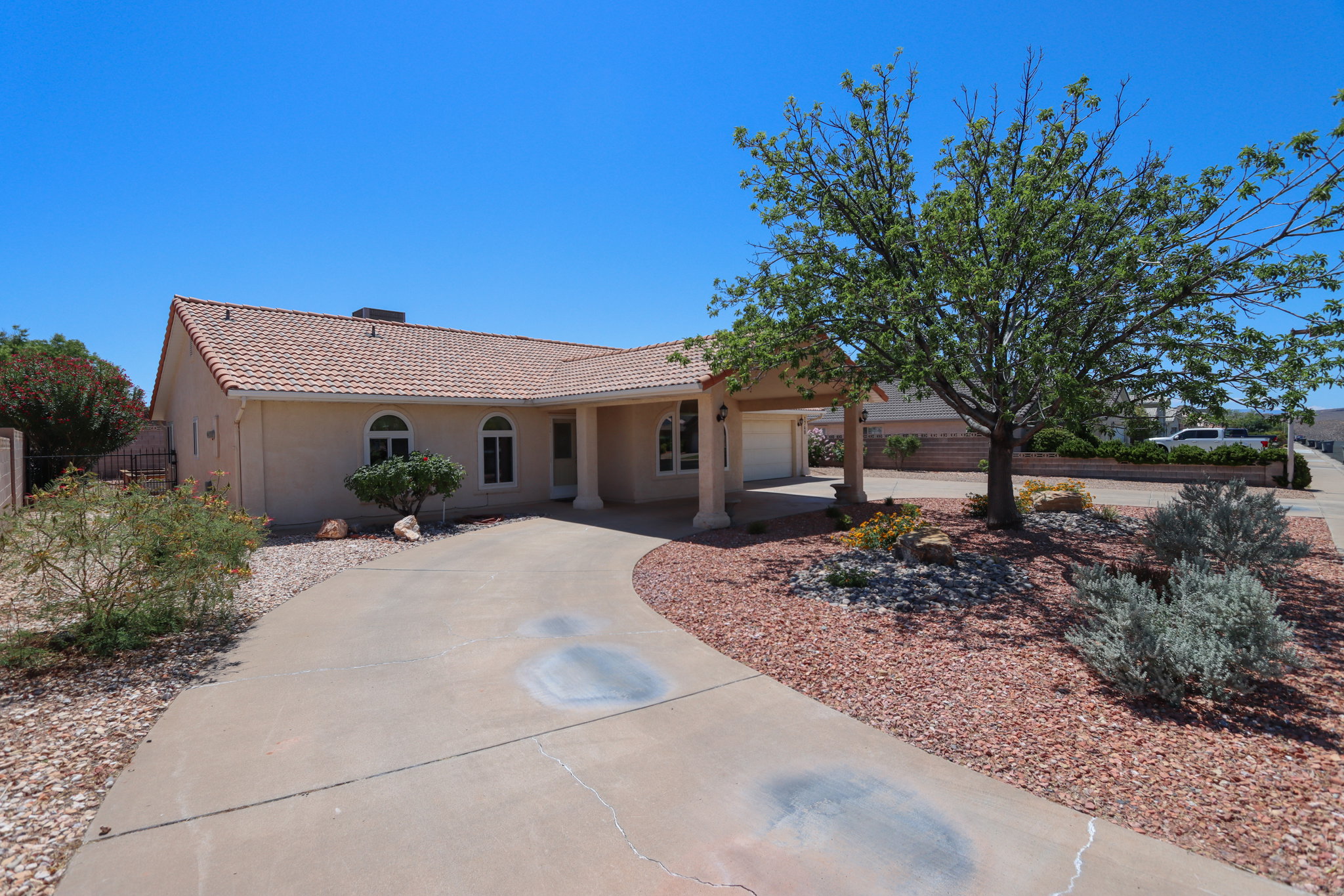 Exterior featuring a tile roof, covered entry, arched windows, an attached two-car garage, and desert-friendly landscaping