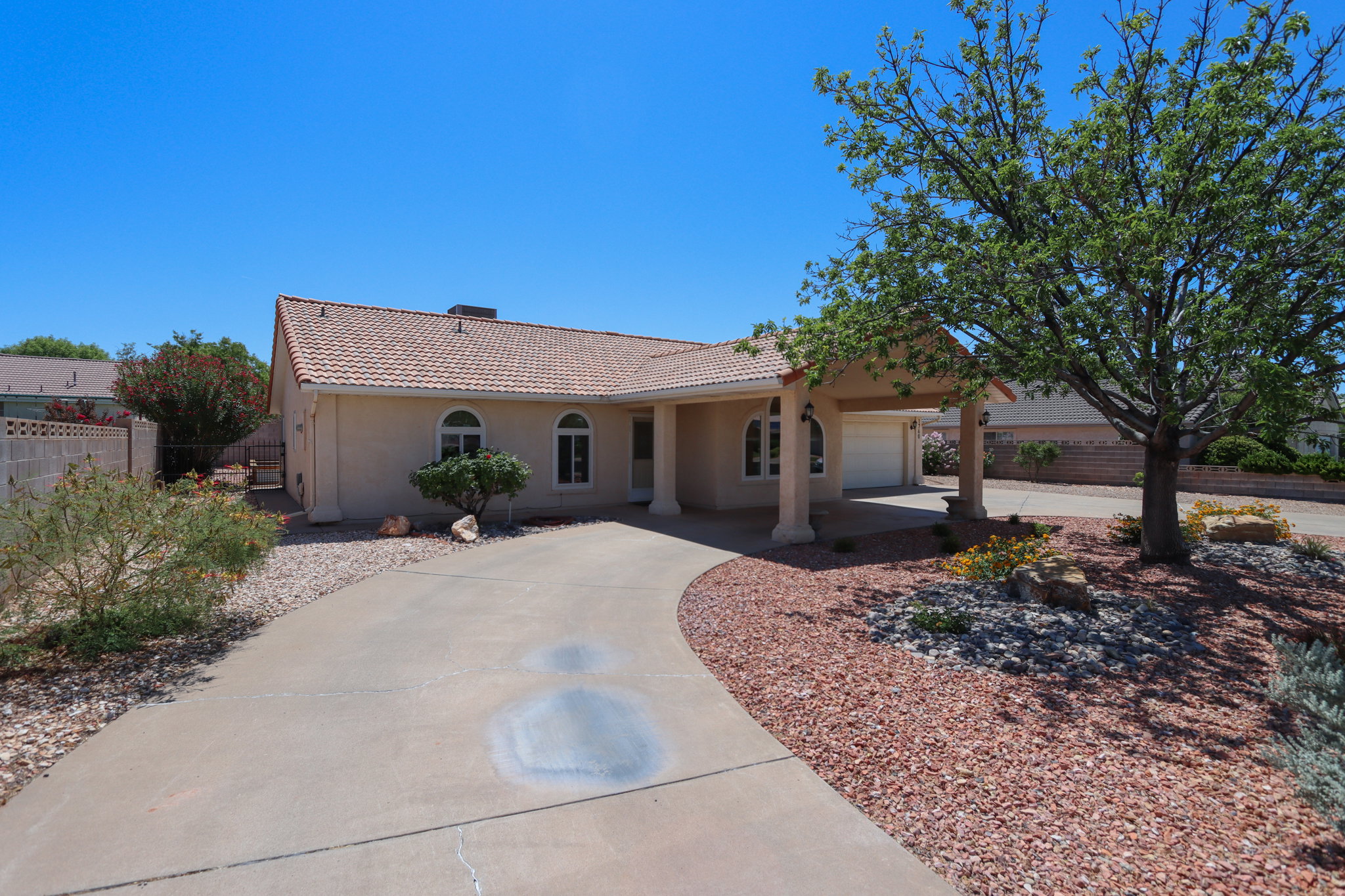 Southwestern-style residence featuring a tile roof, stucco exterior, covered entry with columns, attached garage, and a curved concrete driveway