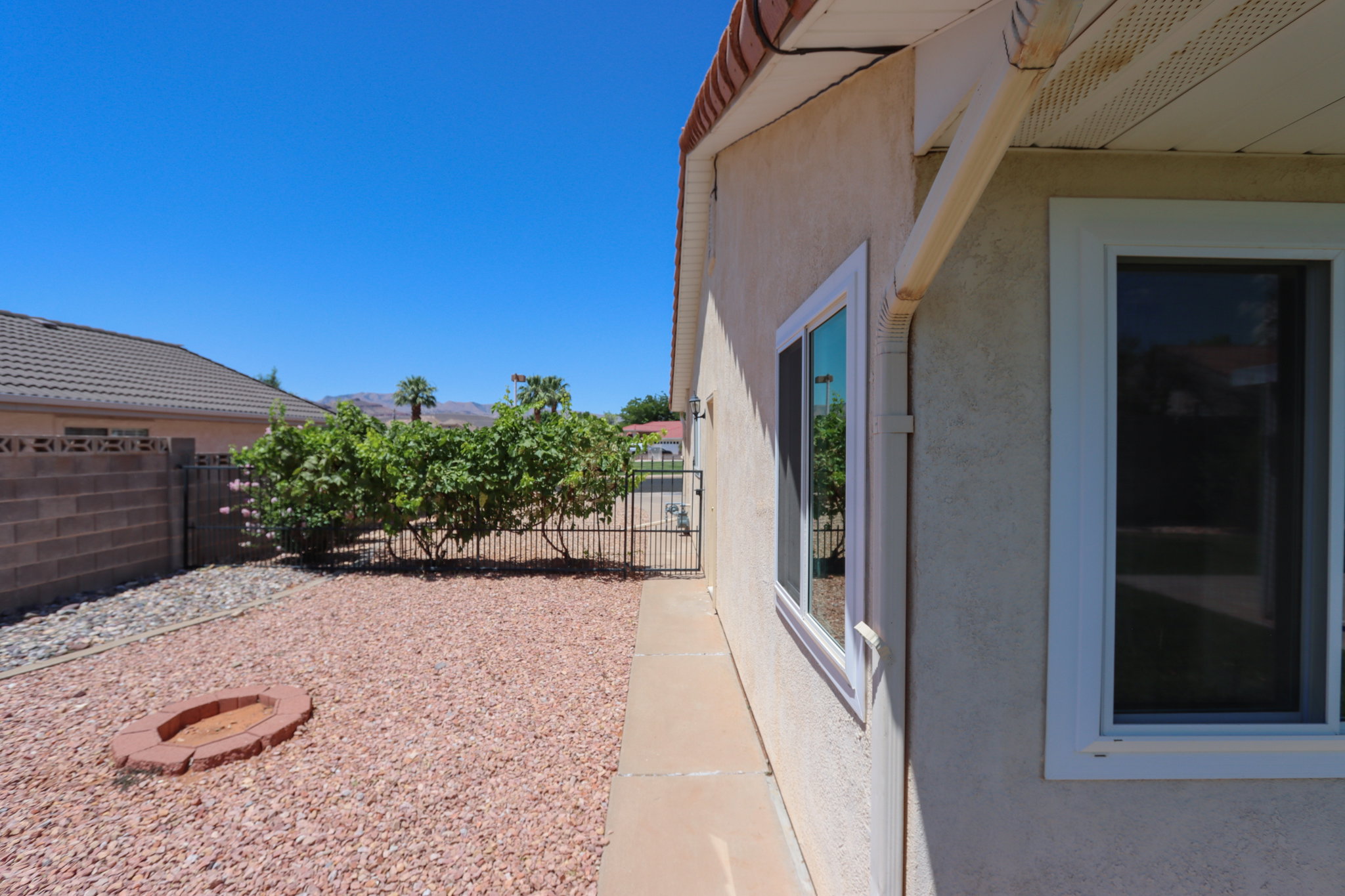 Stucco exterior with multiple windows, concrete walkway, and a rock-covered yard featuring a brick-lined fire pit