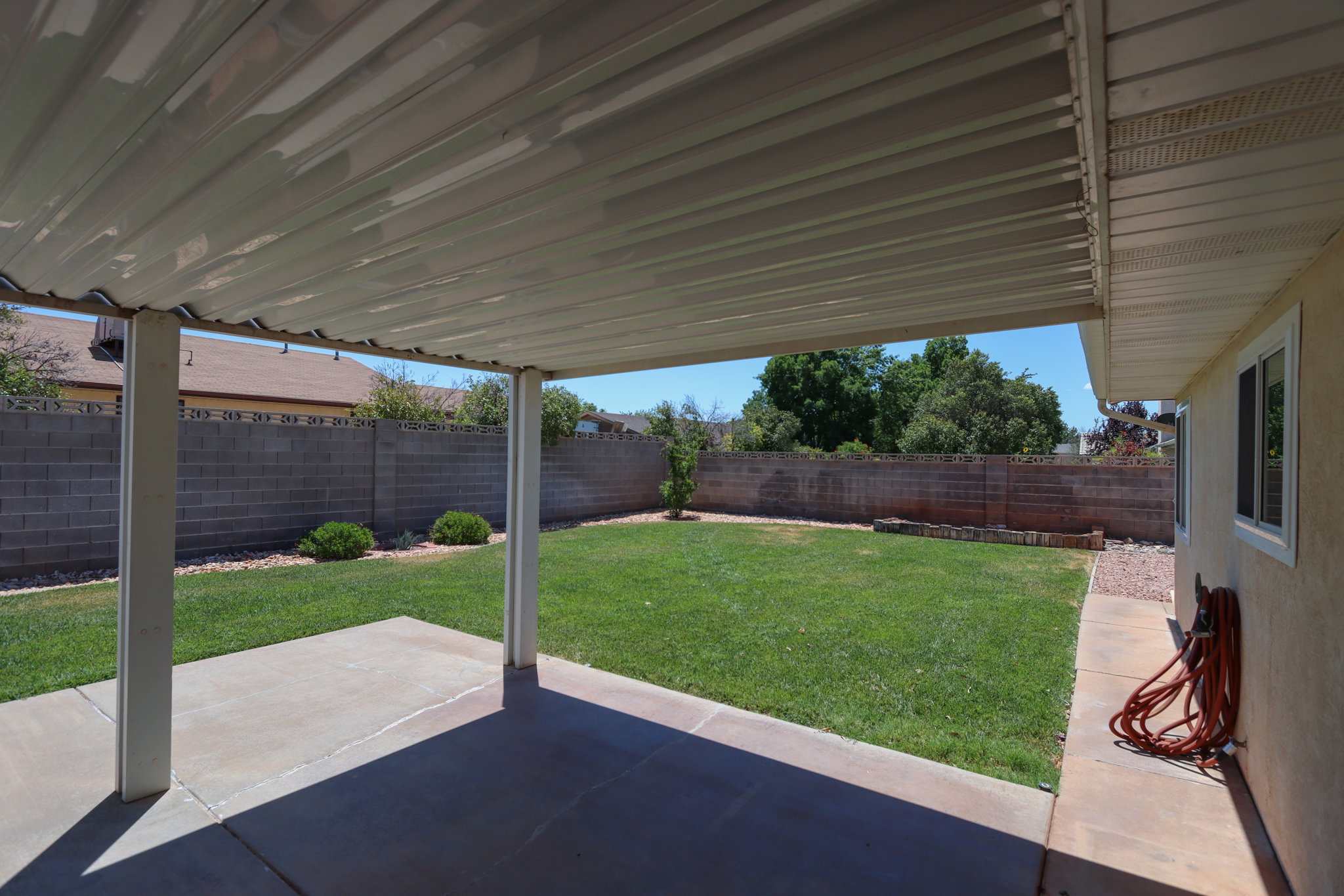 Expansive covered patio featuring a concrete slab, supporting columns, and a corrugated metal roof