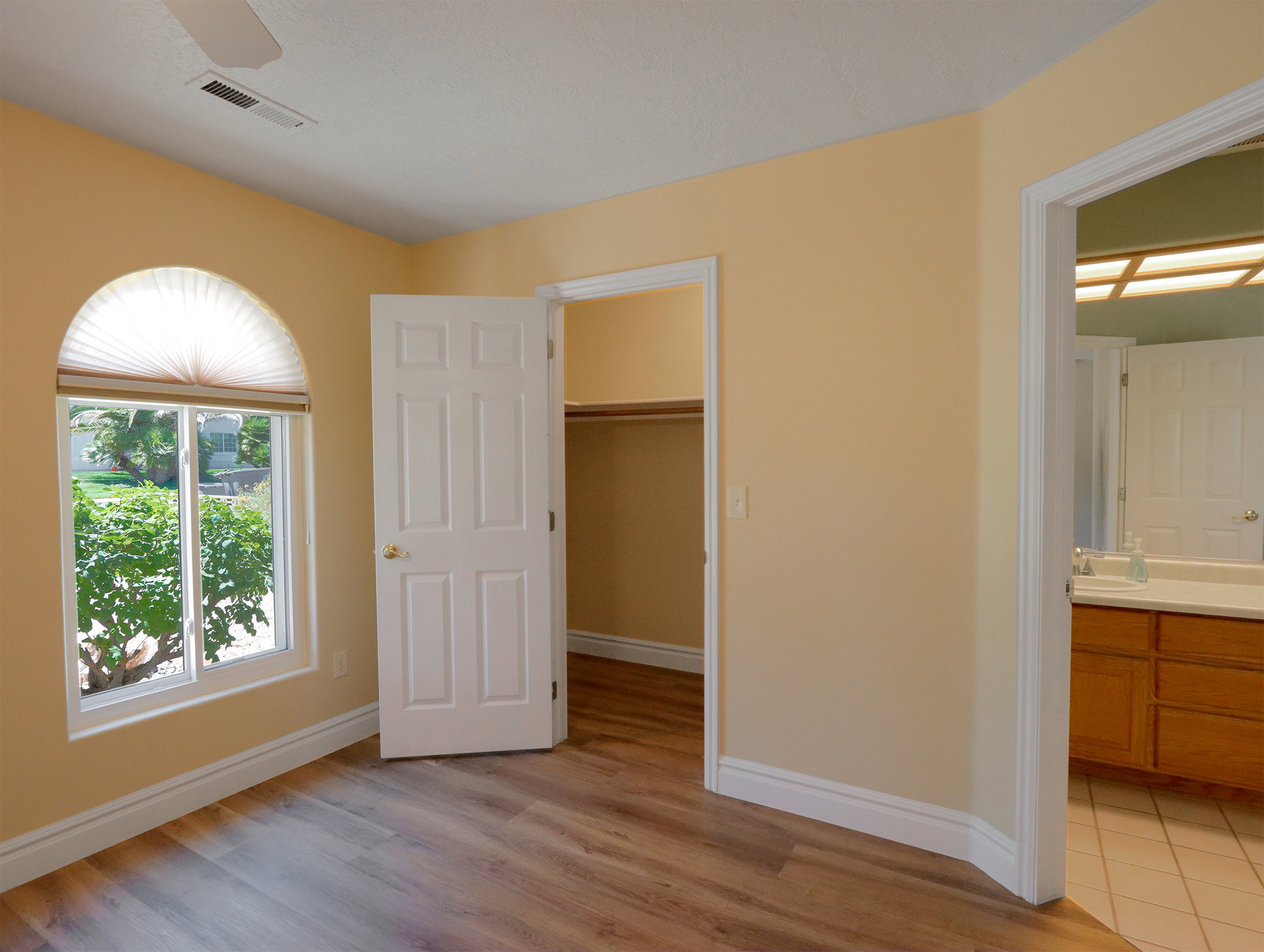 Room featuring wood-finish flooring, a semi-arch window with privacy blinds, and a ceiling fan
