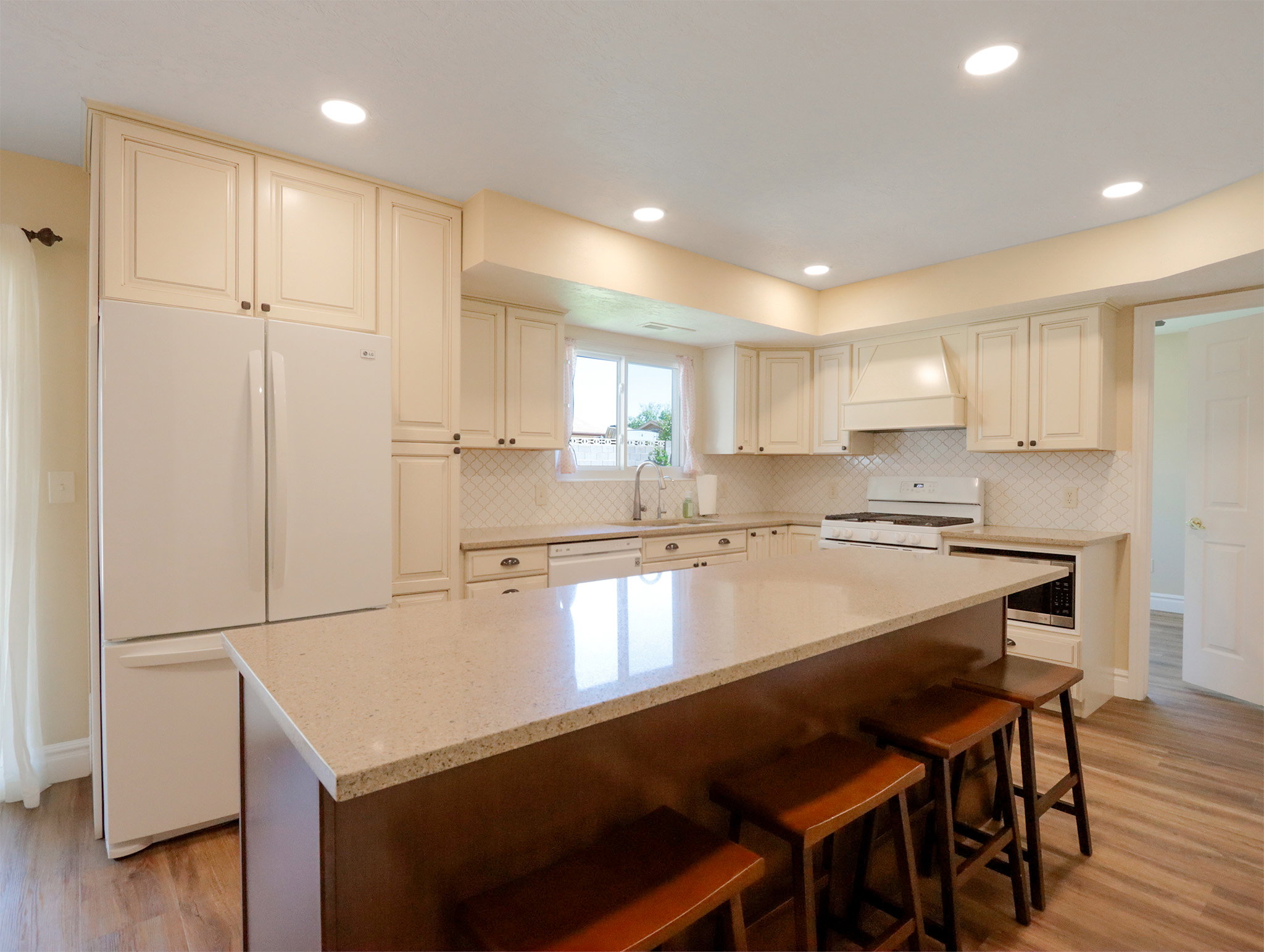Spacious kitchen featuring a large island with a quartz countertop, extensive cabinetry, wood-finish flooring, and recessed lighting