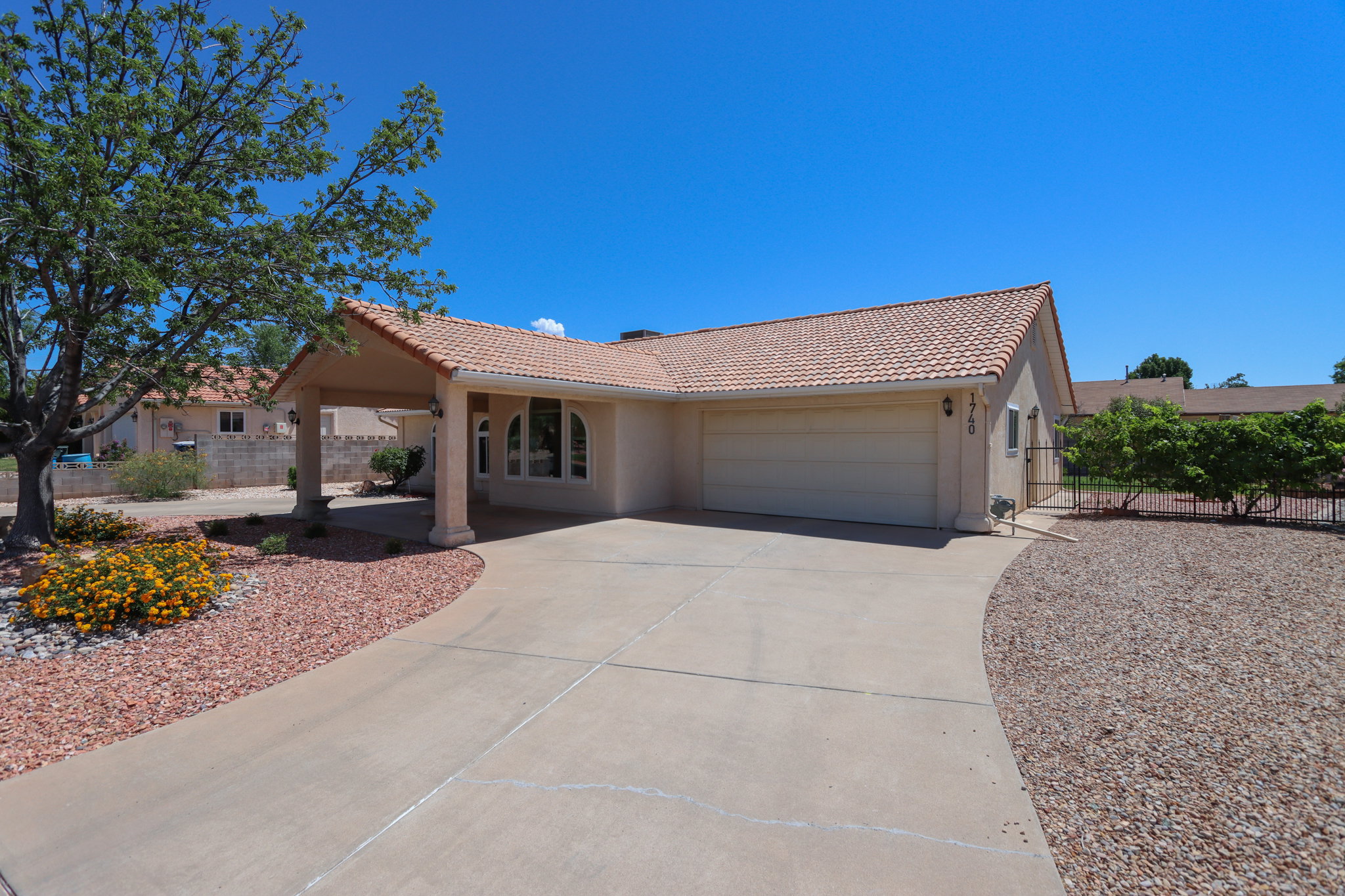 Single-story residence featuring a tile roof, an integrated carport with columns, a two-car garage, and a curved concrete driveway