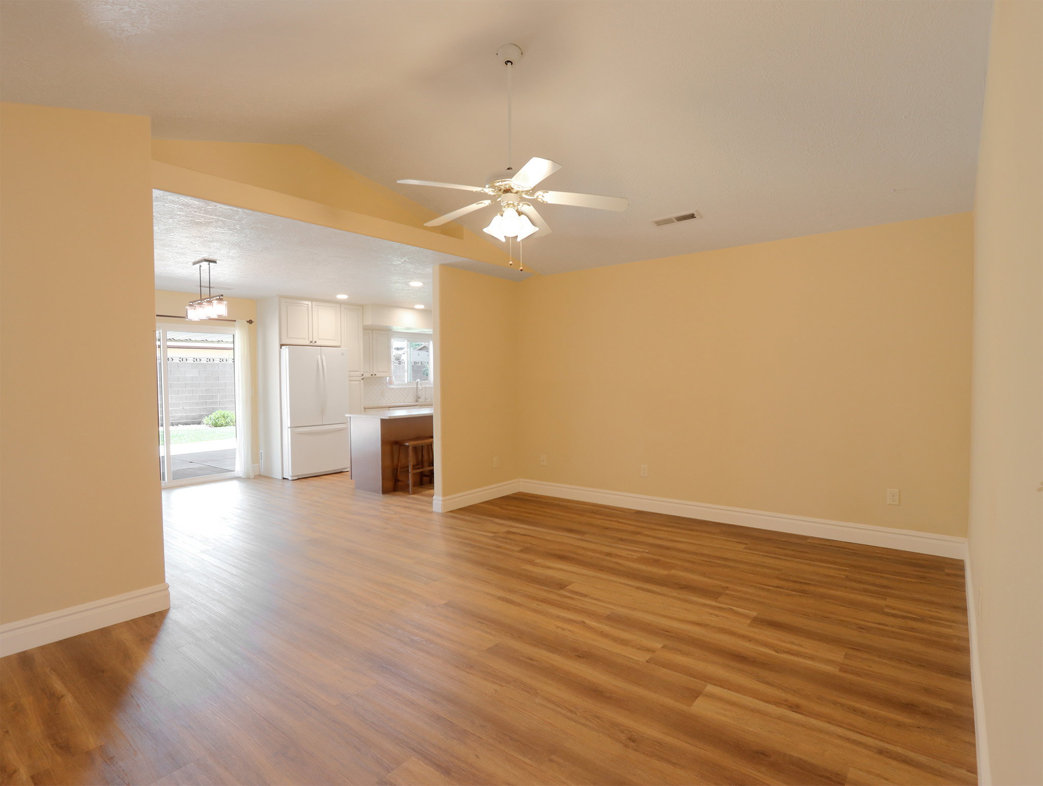 Spacious living area featuring wood-finish flooring, vaulted ceiling, and a ceiling fan