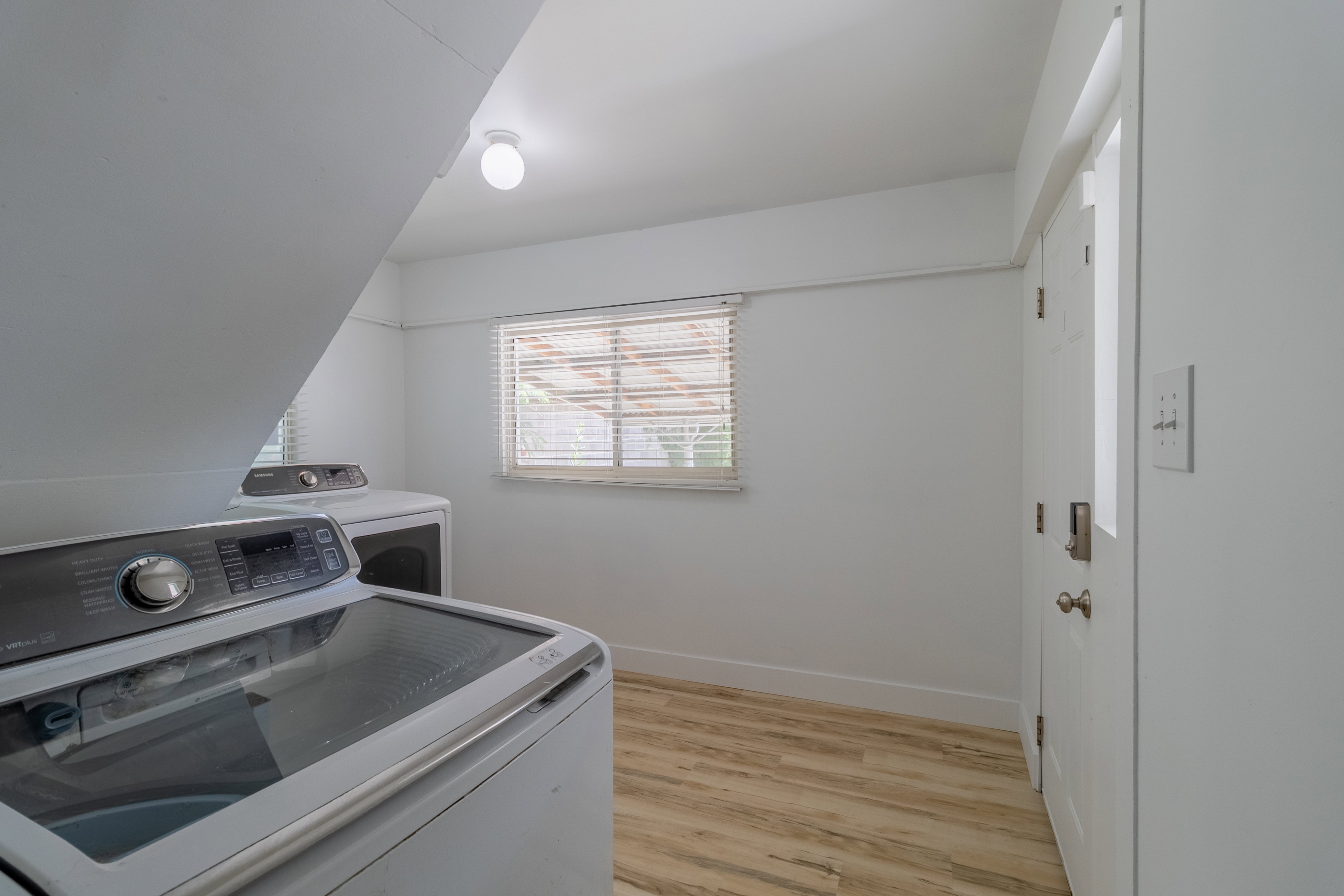 Dedicated laundry area featuring wood-finish flooring and a window with blinds