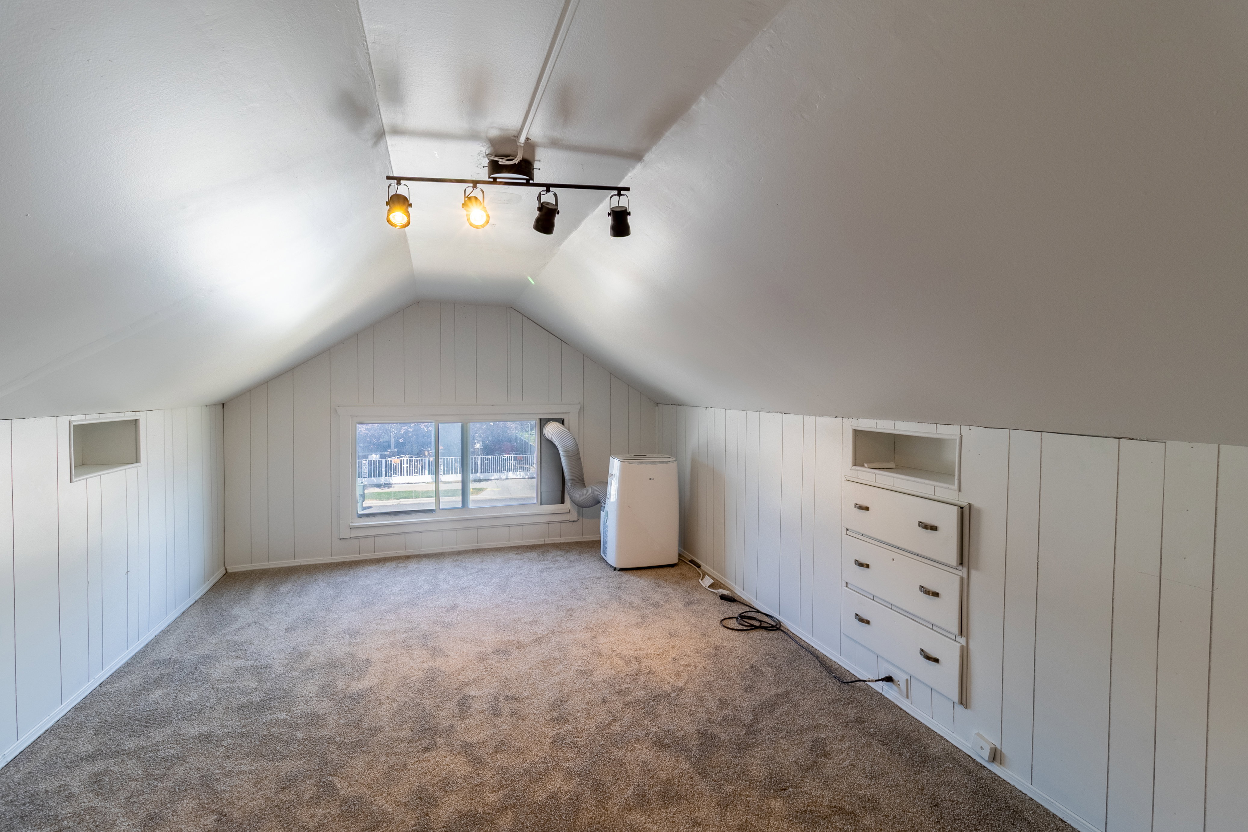 Attic space featuring sloped ceilings, track lighting, built-in storage drawers, and a window