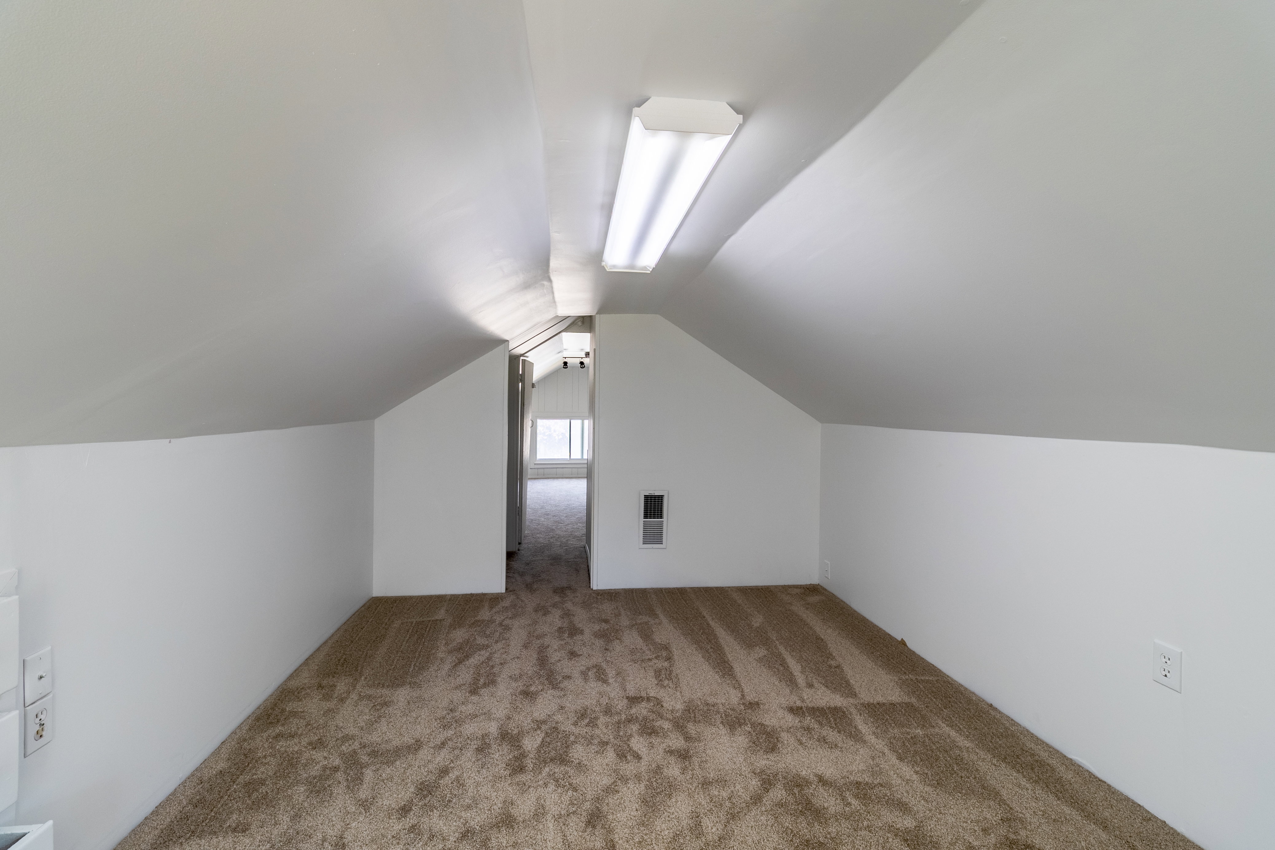 Carpeted attic space featuring sloped ceilings, white painted walls, and a fluorescent ceiling light fixture