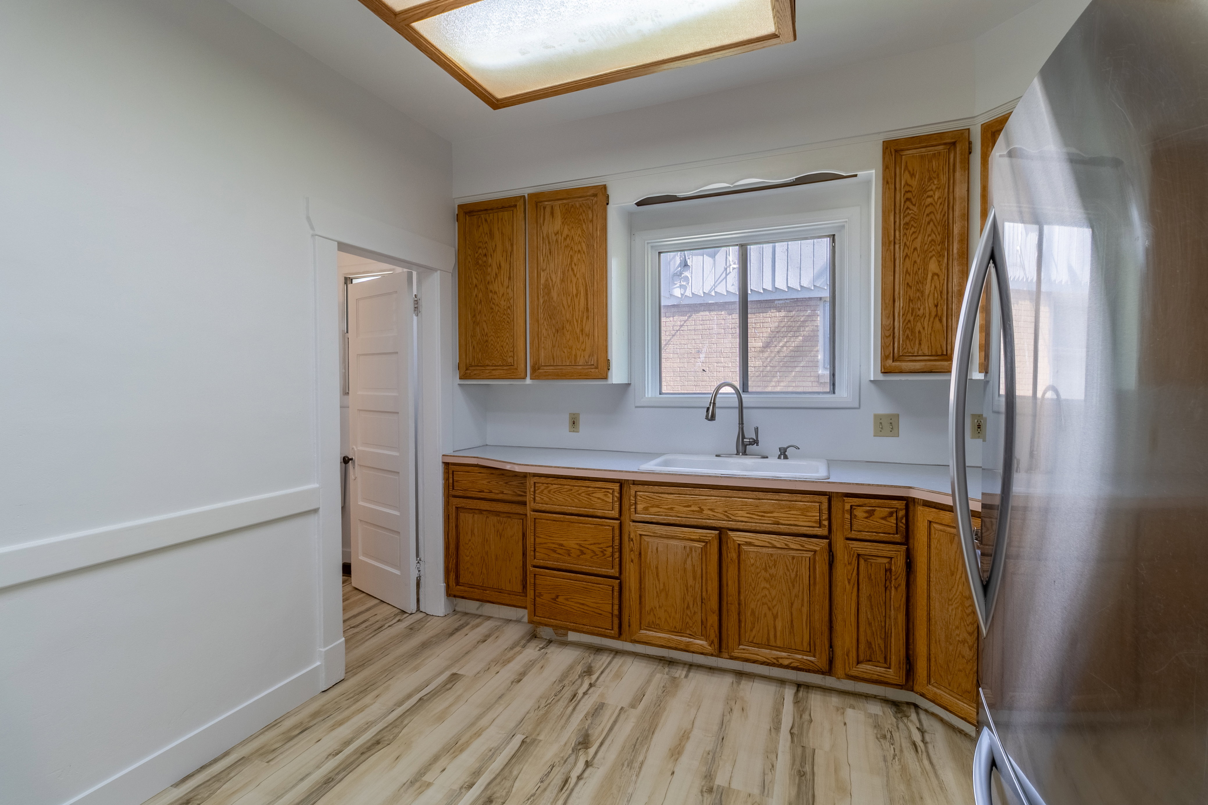 Kitchen featuring wood-finish cabinetry, light-toned countertops, a stainless steel refrigerator, and wood-finish flooring