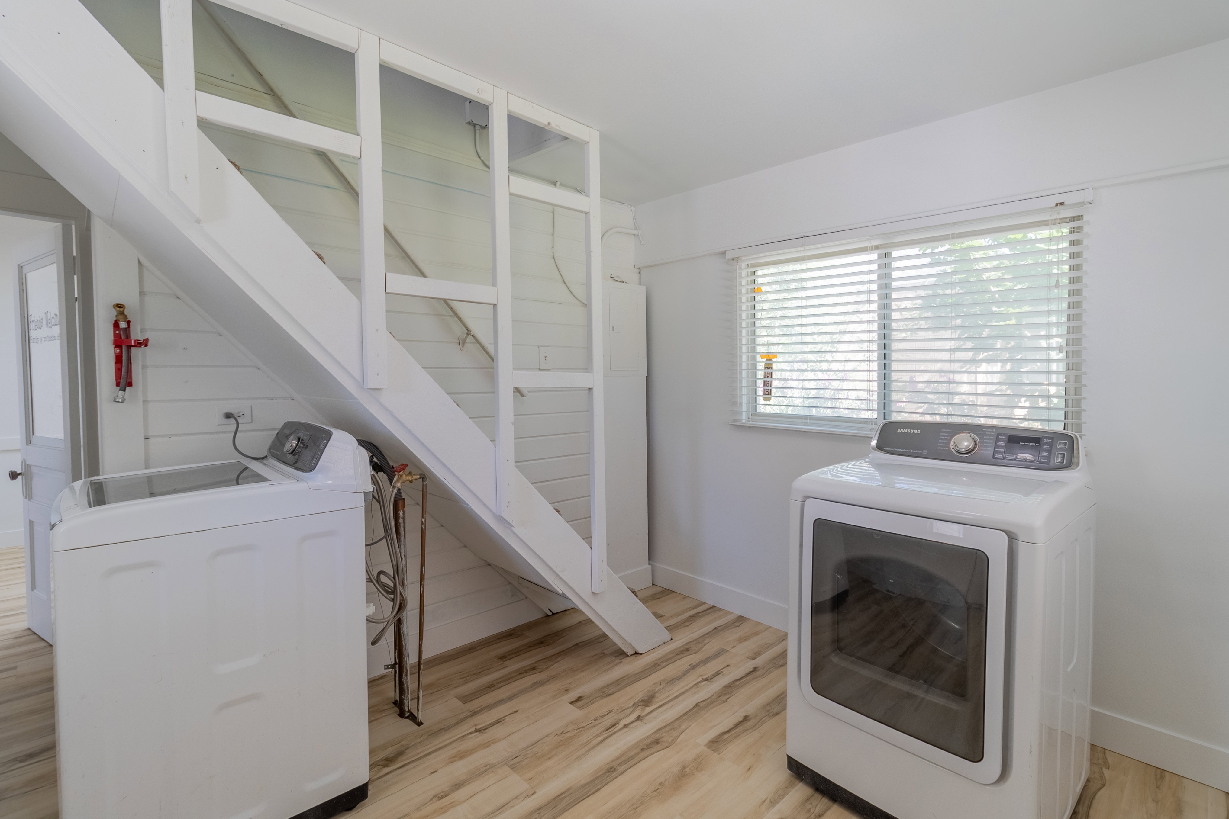 Laundry area with wood-finish flooring, white shiplap wall, and a bright window with blinds