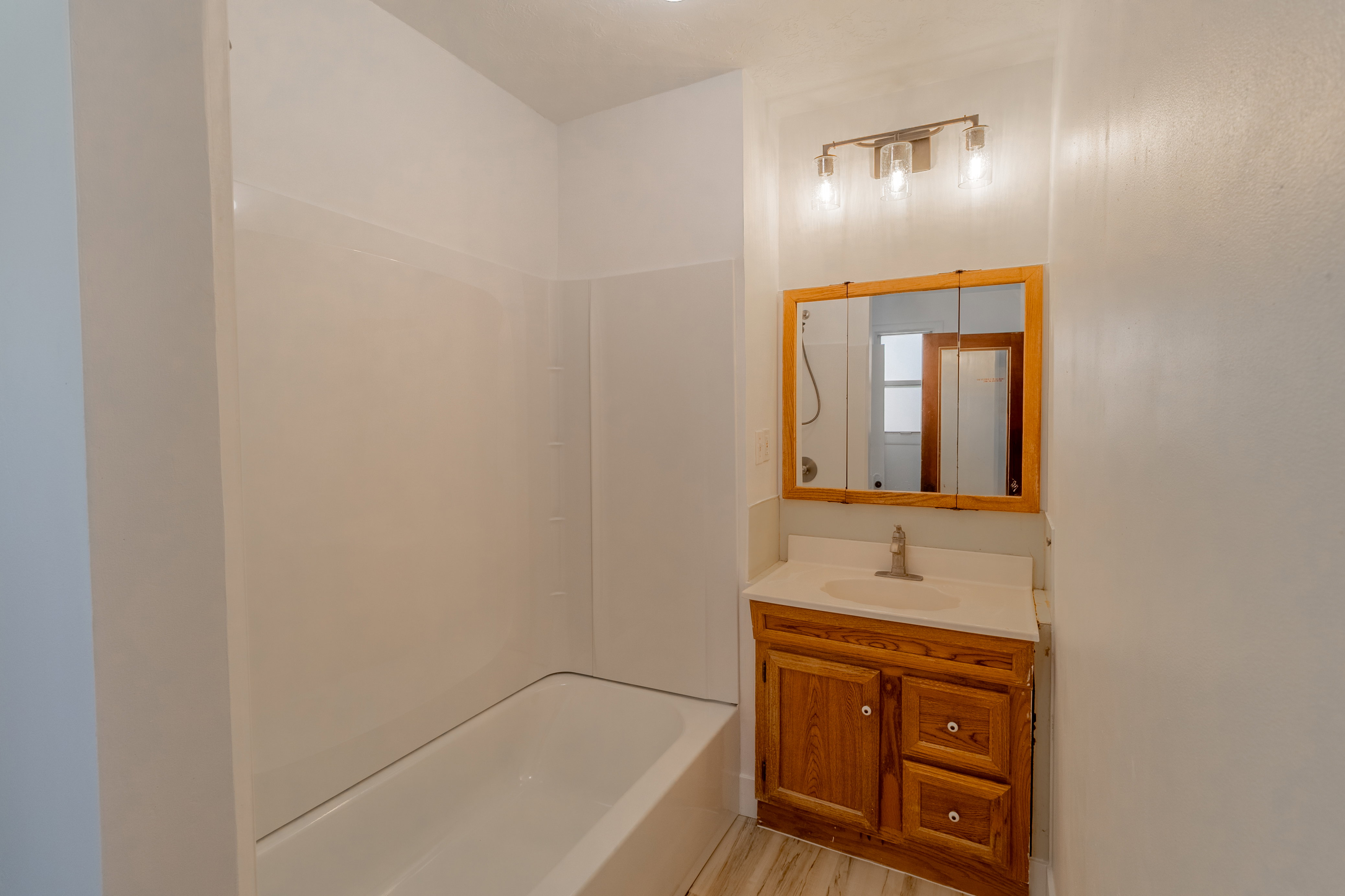 Bathroom featuring a white bathtub, white shower surround, and wood-finish vanity with a single sink