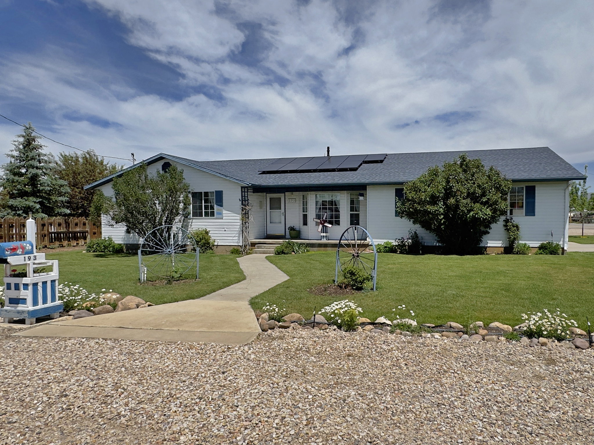 Single-story residence featuring white siding, a dark shingle roof with solar panels, and blue window shutters