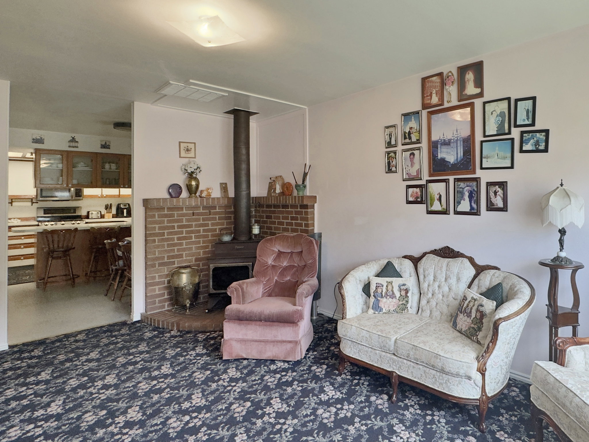 Living area featuring a brick hearth with a wood-burning stove, patterned carpeting, and a ceiling-mounted light fixture