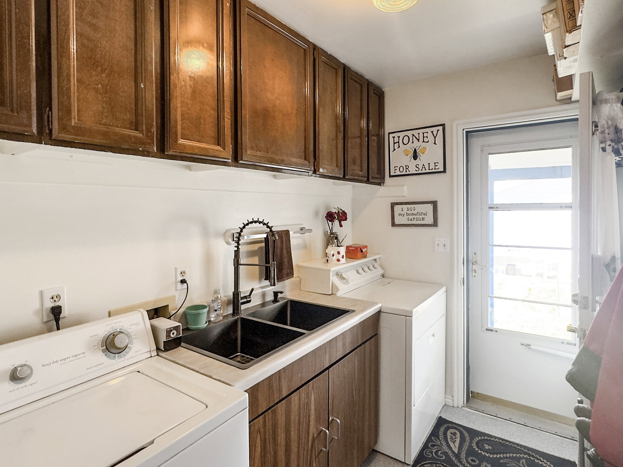 Utility room featuring wood-finish cabinetry, a double basin sink with a matte black faucet, and a white countertop