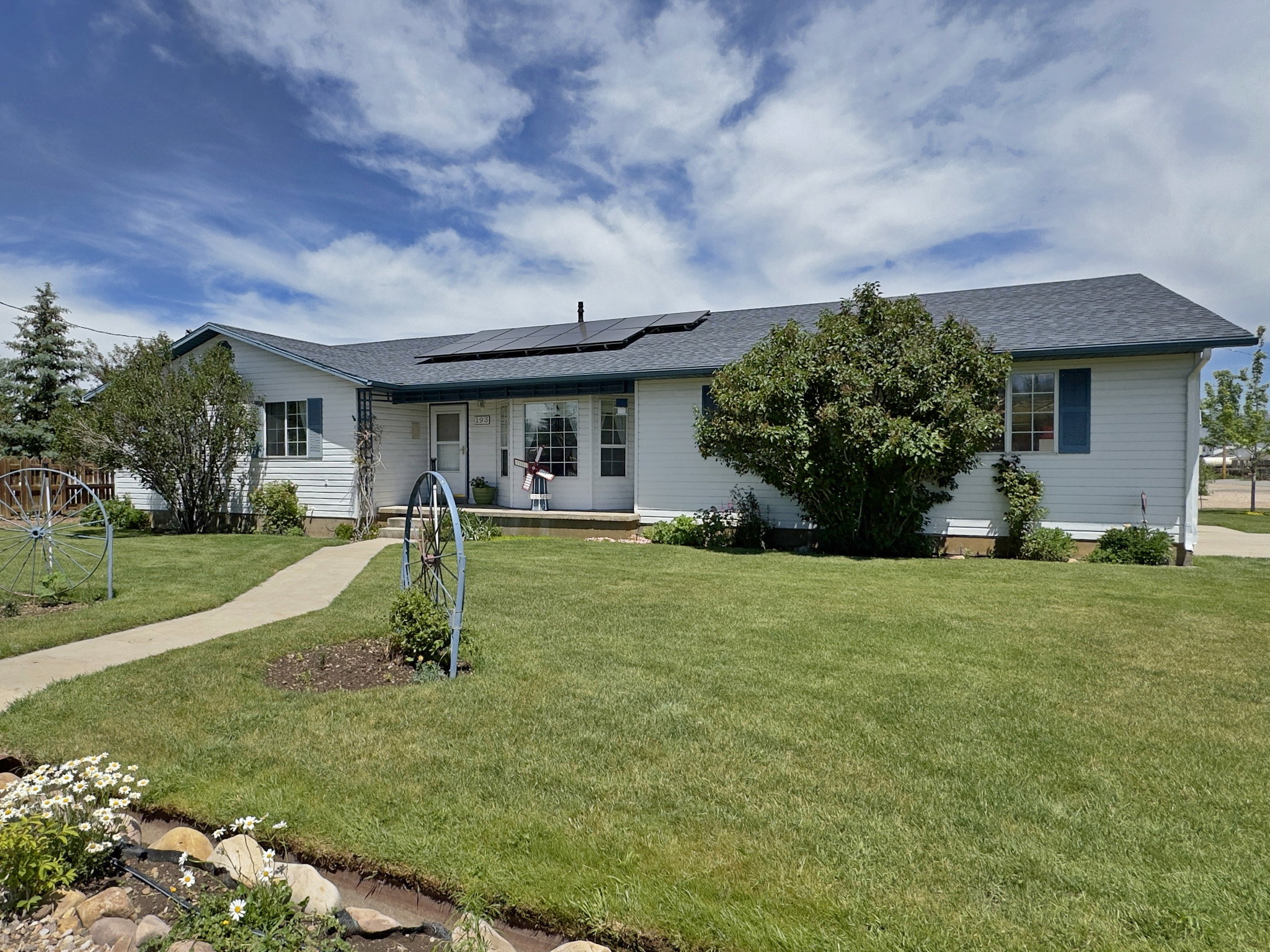 Single-story residence featuring white siding, a dark shingle roof with solar panels, and blue window shutters