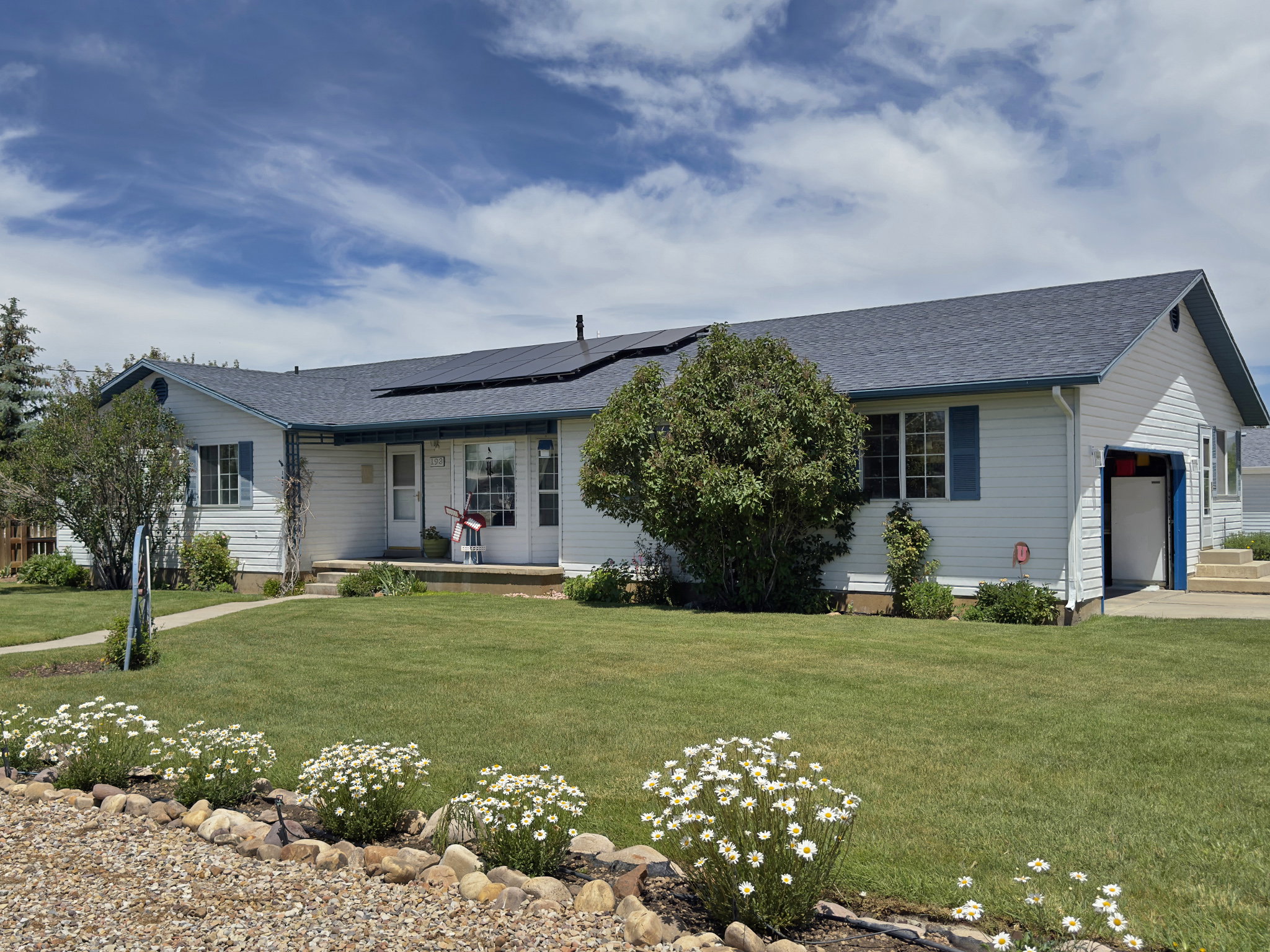 White siding residence featuring a dark shingled roof with solar panels