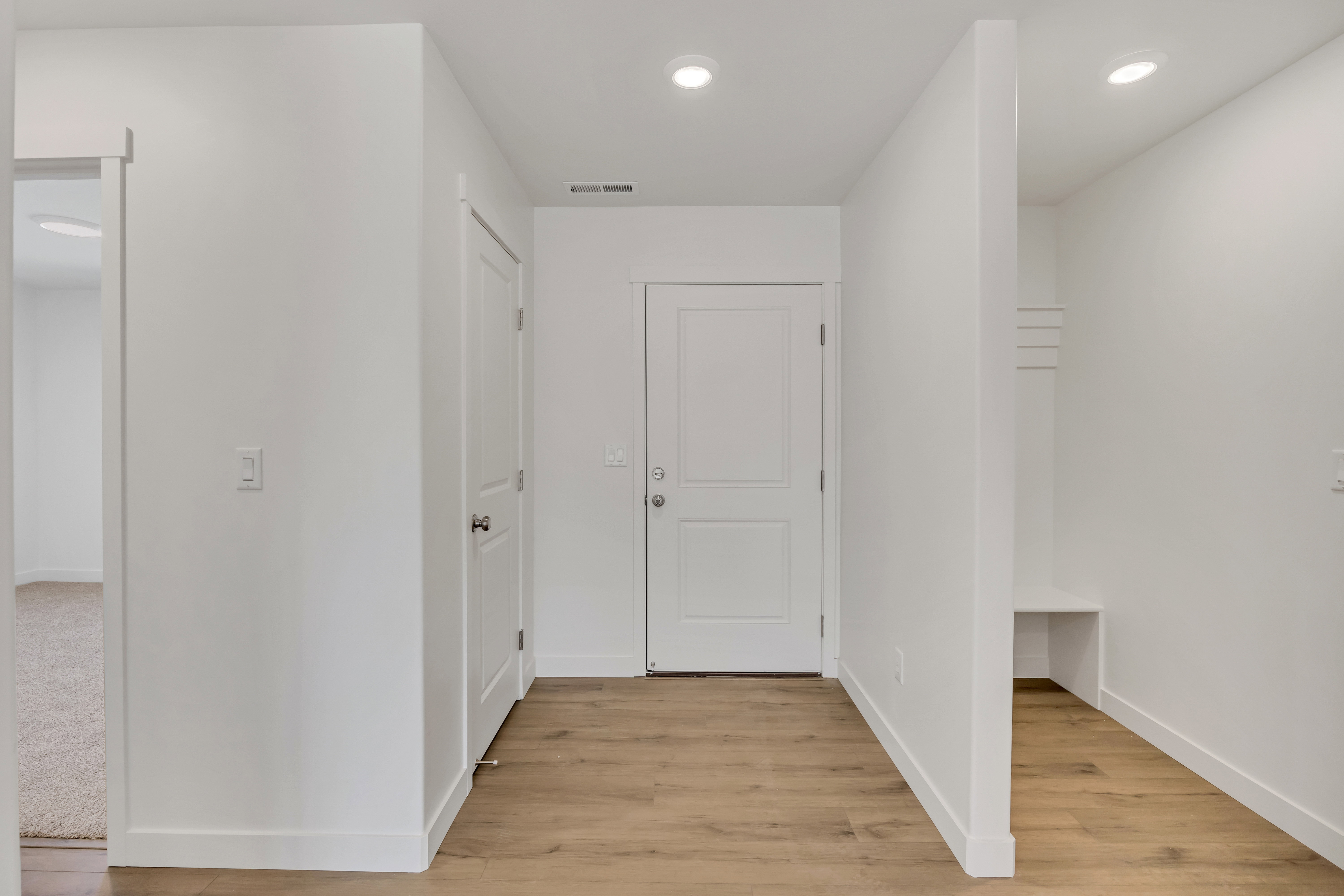 Entryway featuring wood-finish flooring, recessed lighting, white panel doors, and a built-in bench with coat hooks