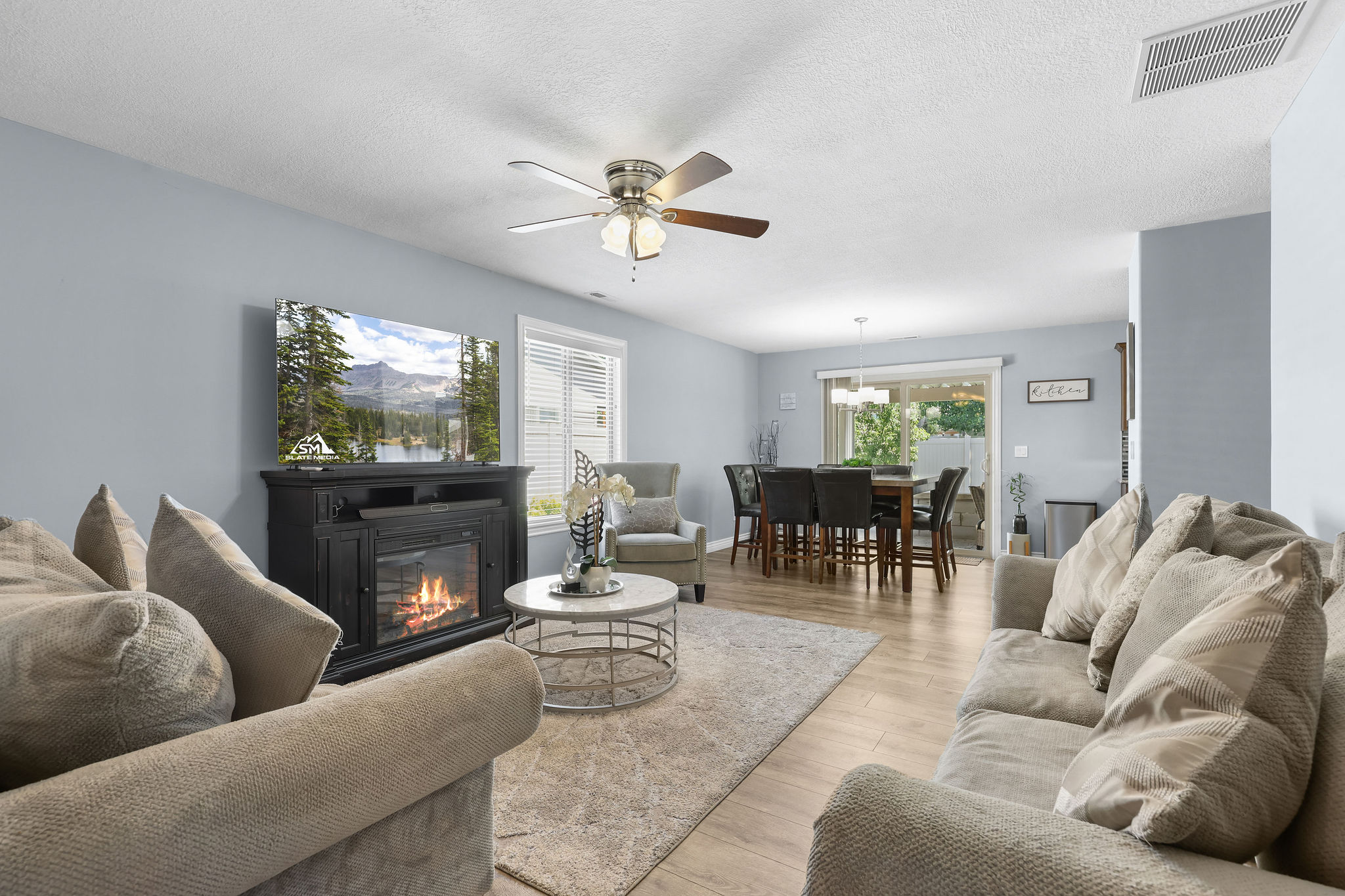 Bright living area featuring wood-finish flooring, a built-in fireplace media console, and a ceiling fan with integrated lighting