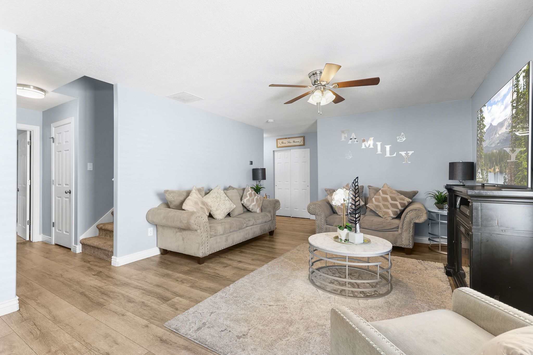 Expansive living area with wood-finish flooring, light blue walls, and a ceiling fan