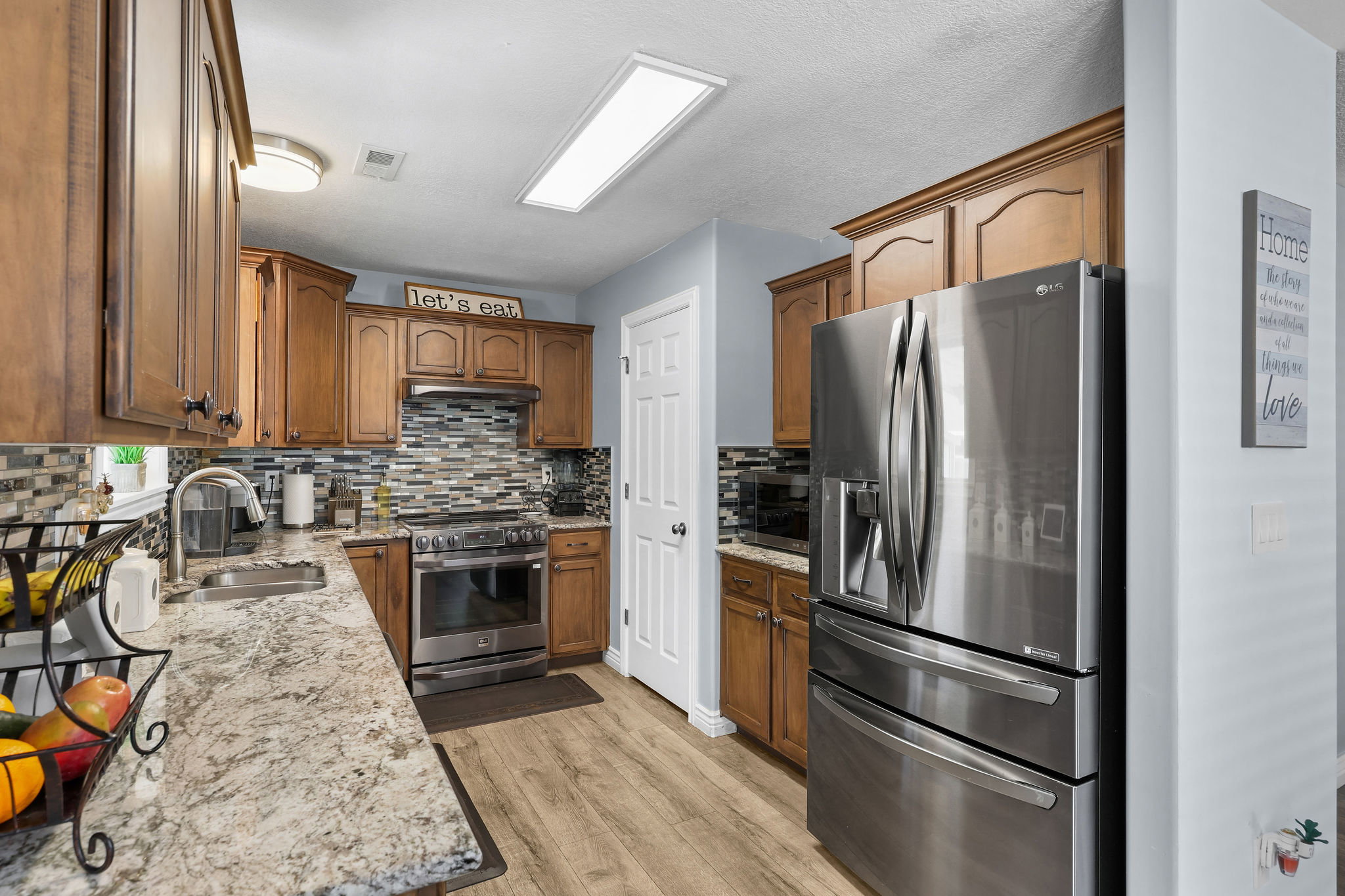 Kitchen featuring wood-finish cabinetry, granite-style countertops, a mosaic tile backsplash, and stainless steel appliances