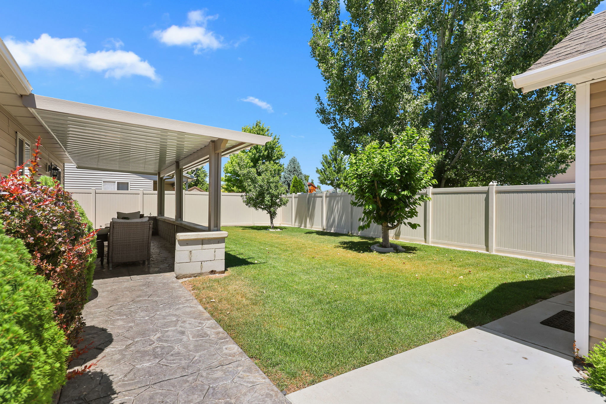 Spacious outdoor patio with a permanent overhead cover, featuring a stamped concrete surface, a built-in block planter, and privacy fencing