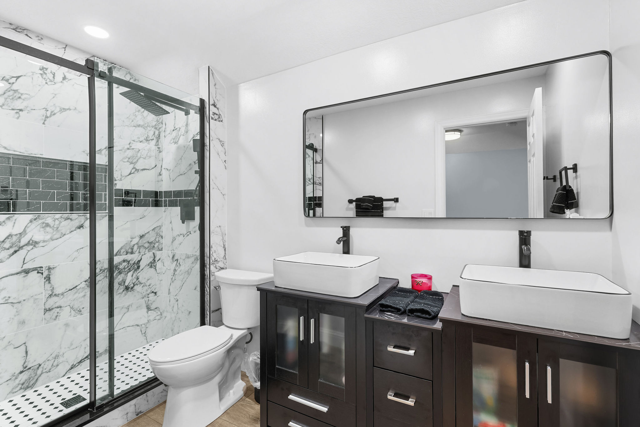 Contemporary bathroom featuring a spacious walk-in shower with black-framed glass enclosure, white marble-style wall tiling, and a contrasting dark mosaic accent band