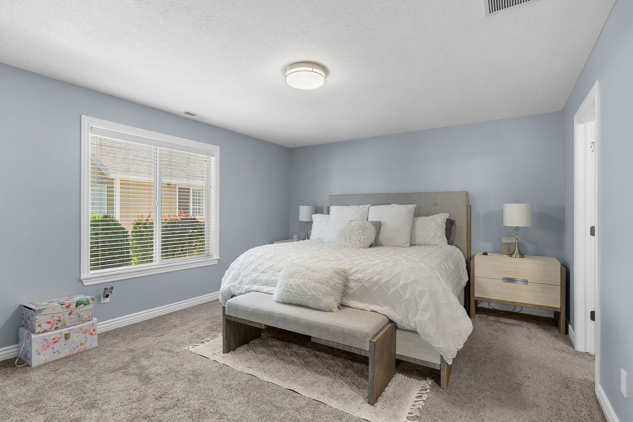 Bedroom featuring plush carpeting, a large window with white blinds, and a built-in overhead light fixture