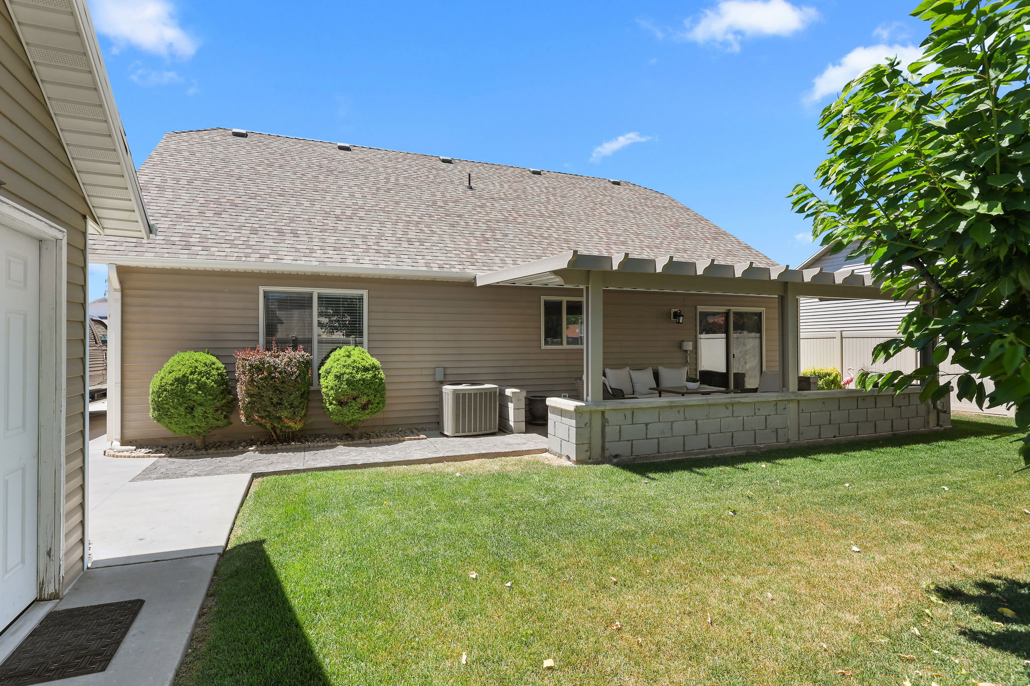 Rear exterior featuring a covered patio with a concrete block privacy wall, a manicured lawn, and mature landscaping