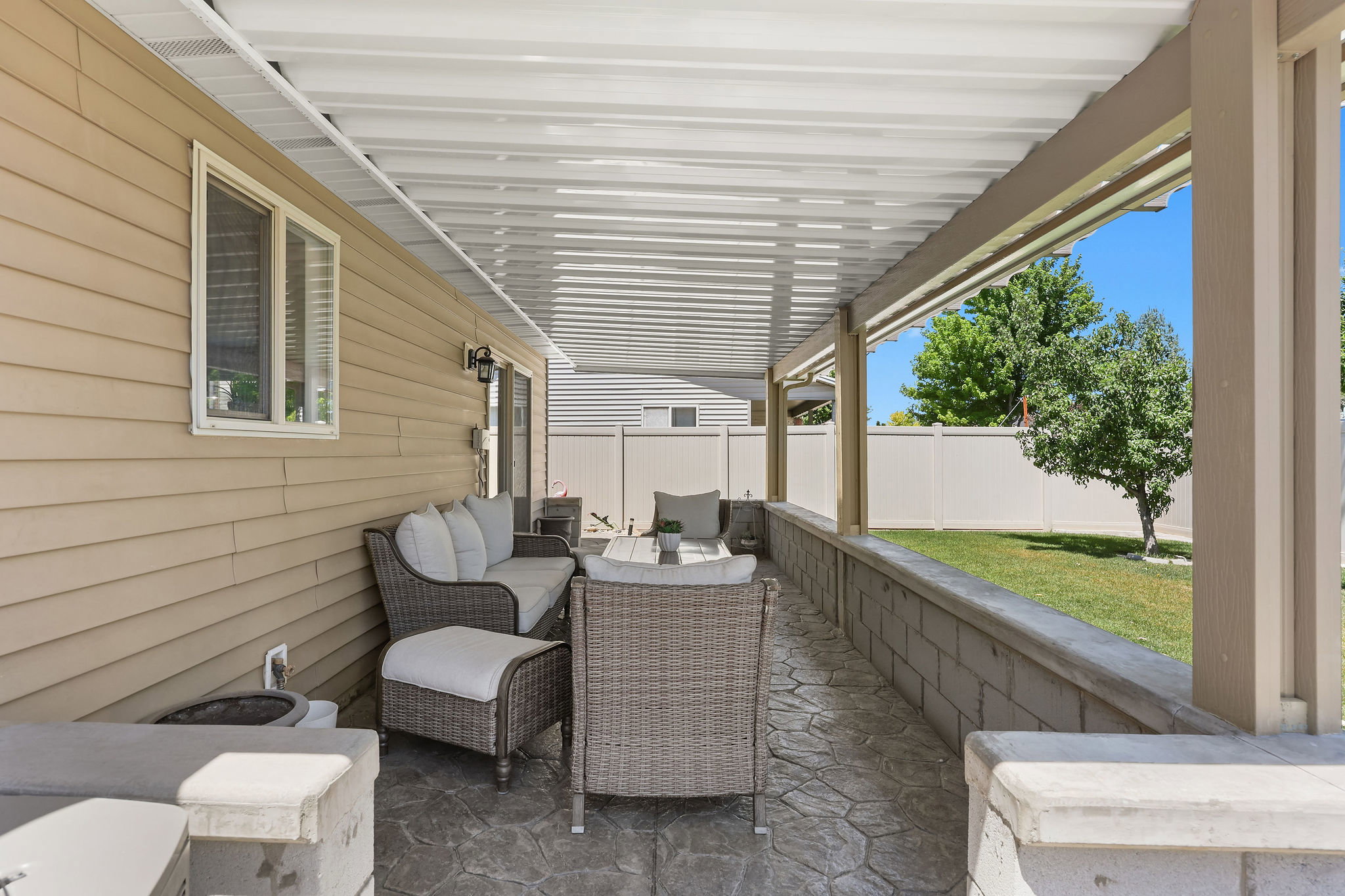 Covered patio with stamped concrete flooring, a horizontal privacy fence, and a block retaining wall