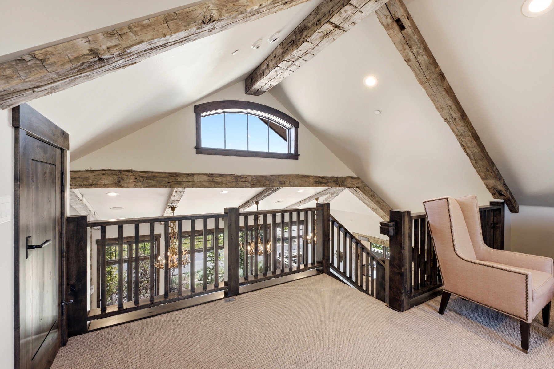 Upper-level landing featuring a vaulted ceiling with exposed wood beams, a custom arched window, and dark wood railings overlooking the level below
