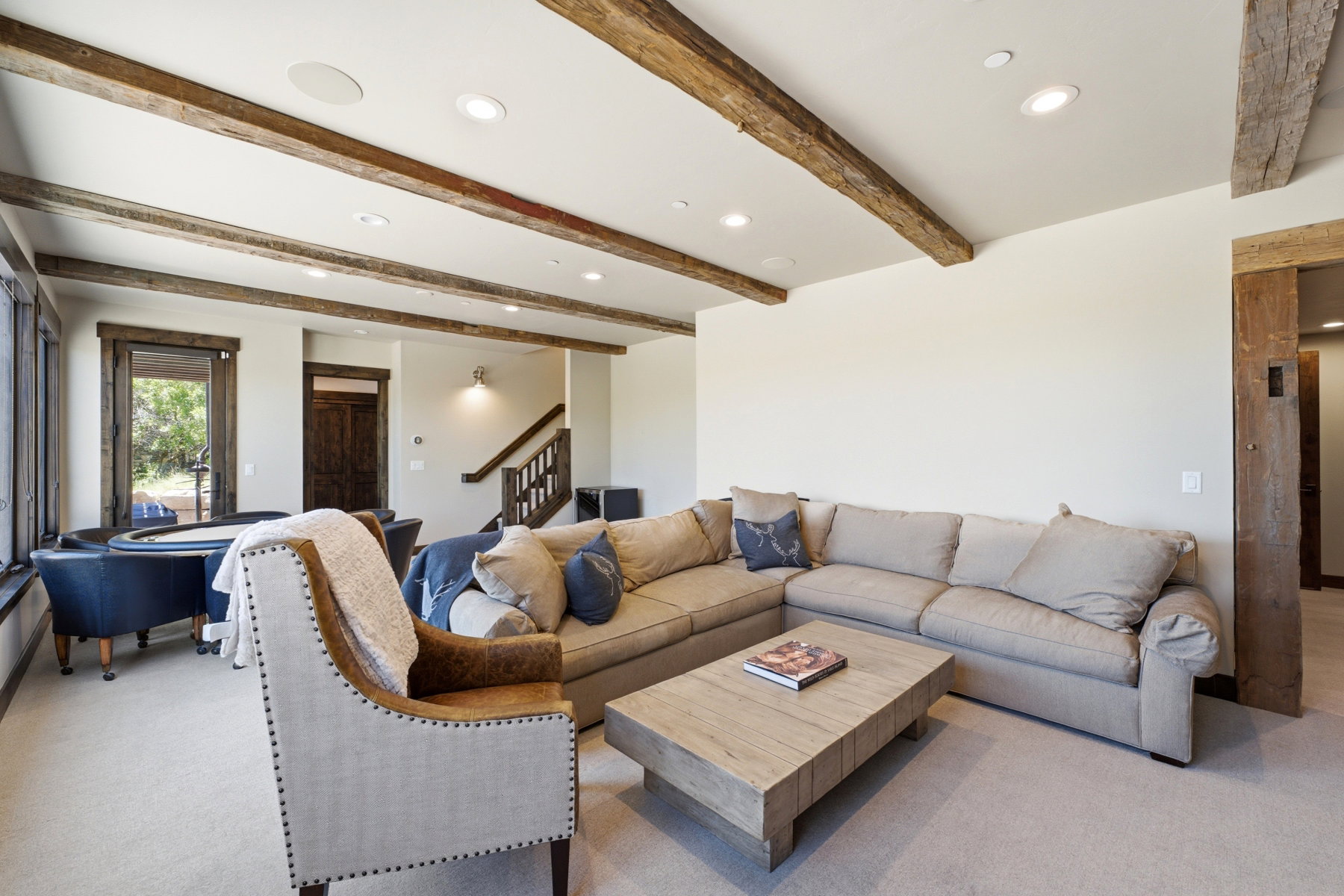 Spacious living area featuring exposed wood beams, recessed lighting, carpeted flooring, and a large window