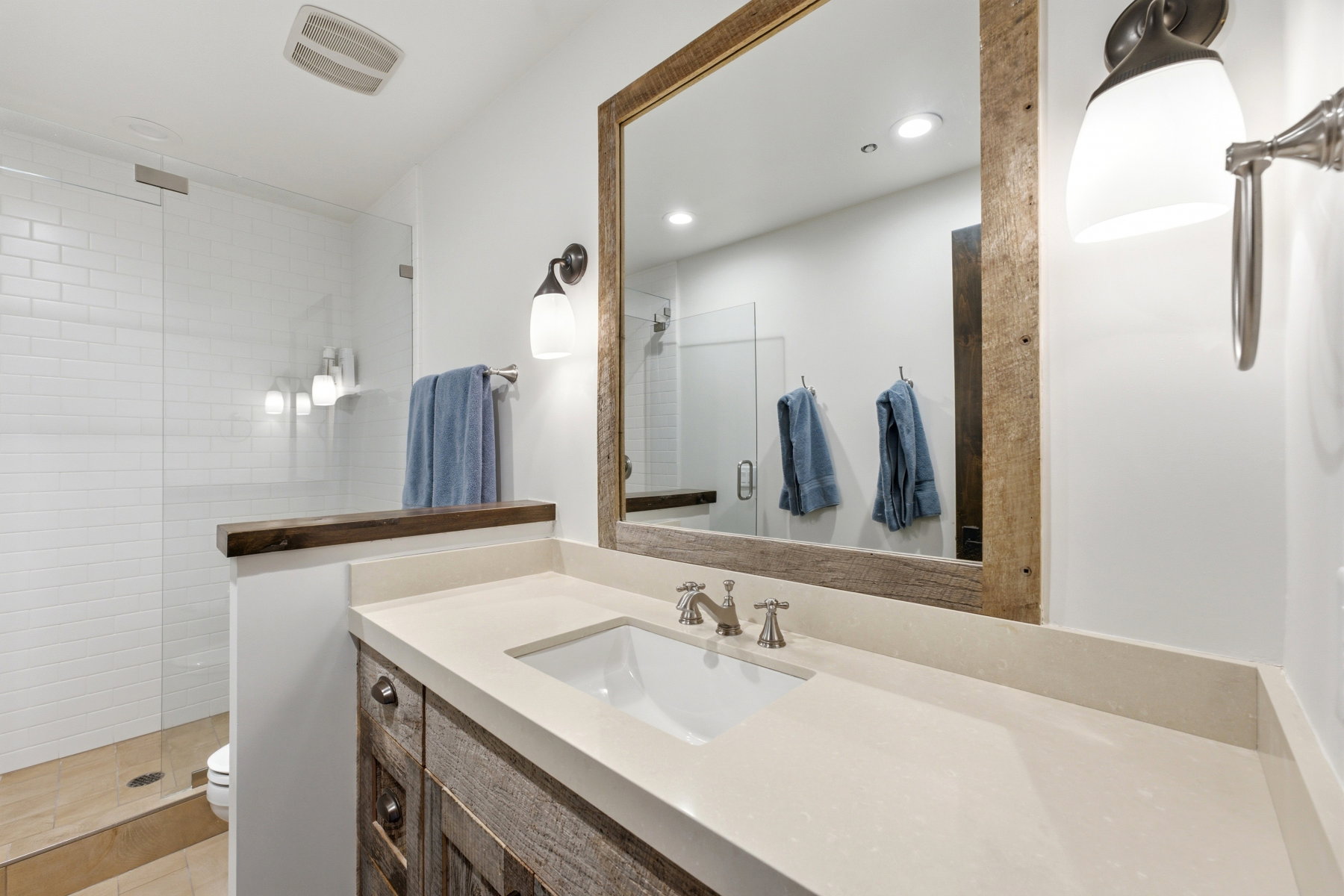 Bathroom vanity featuring a light-toned countertop, under-mount sink, and wood-finish cabinetry