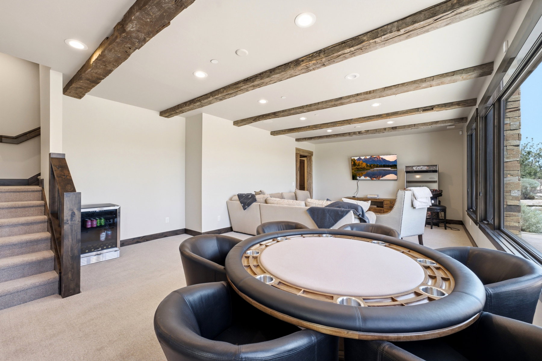 Carpeted lower-level room featuring exposed wood ceiling beams, recessed lighting, and a beverage cooler